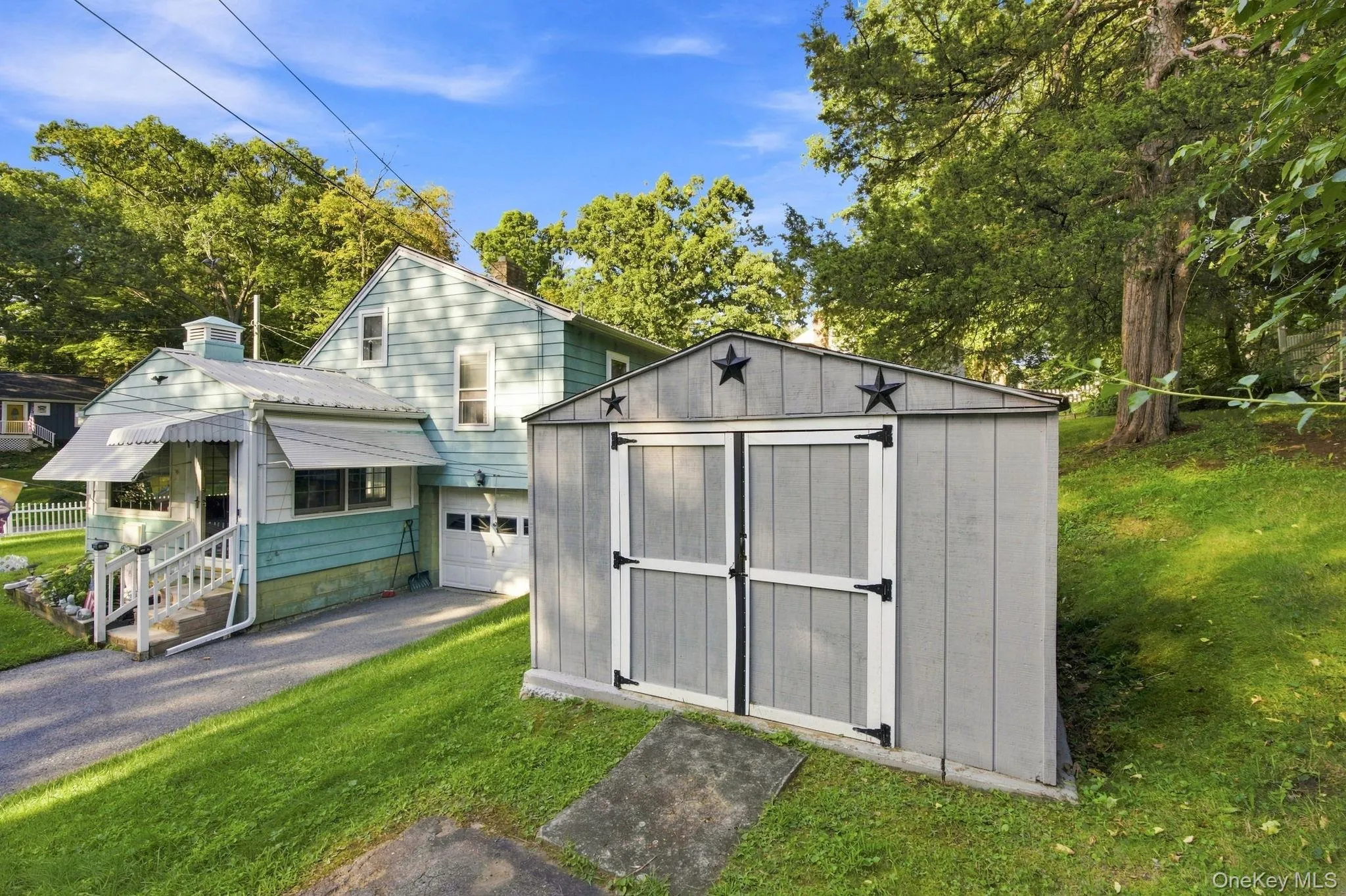 Two-story residence with Turquoise siding, an attached garage, and a covered porch with white railings and metal shed. Two-story residence with Turquoise siding, an attached garage, and a covered porch with white railings and metal shed.