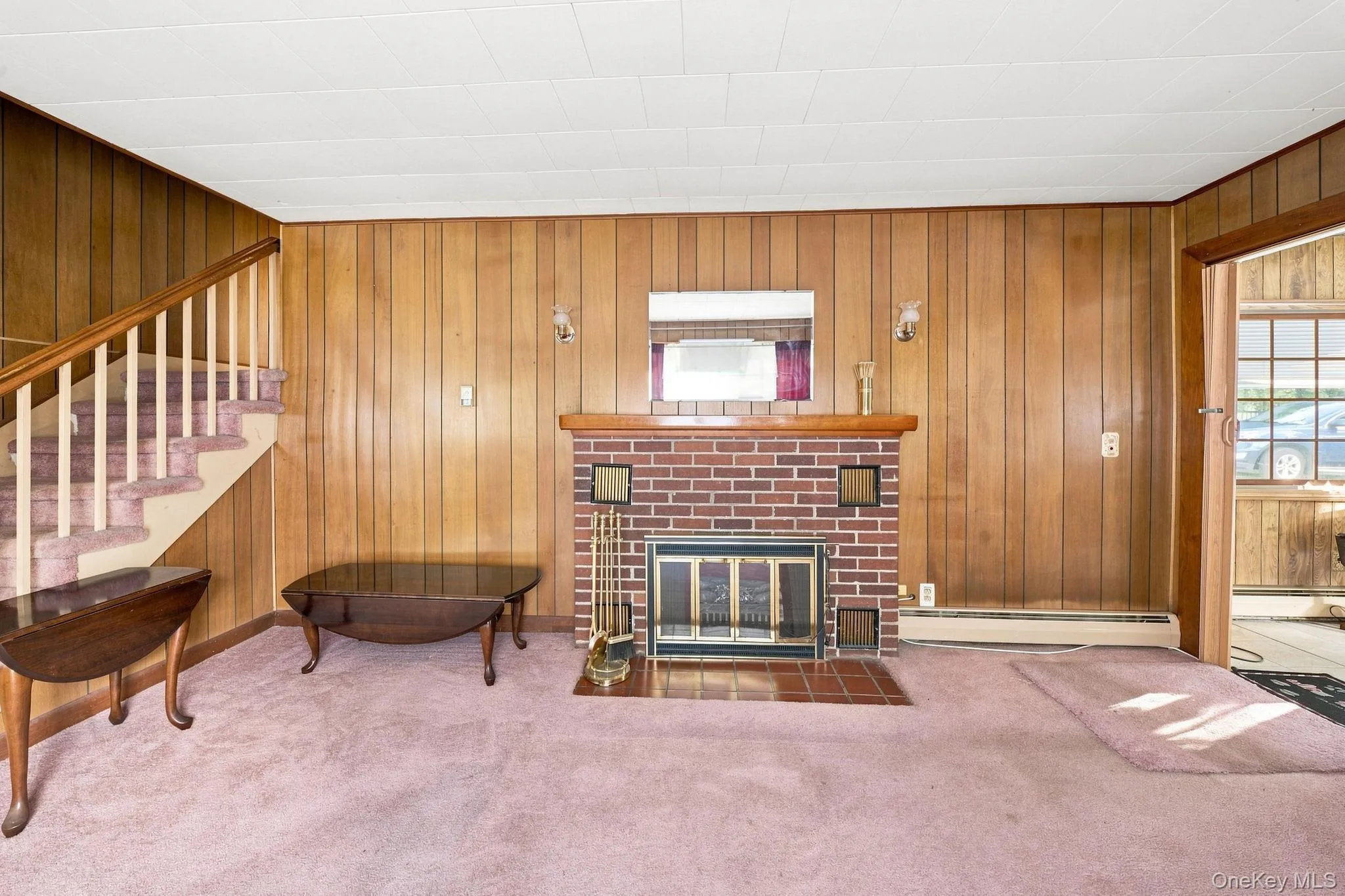 Wood paneling throughout, brick fireplace with a wood mantle, and a staircase with a wood railing Wood paneling throughout, brick fireplace with a wood mantle, and a staircase with a wood railing