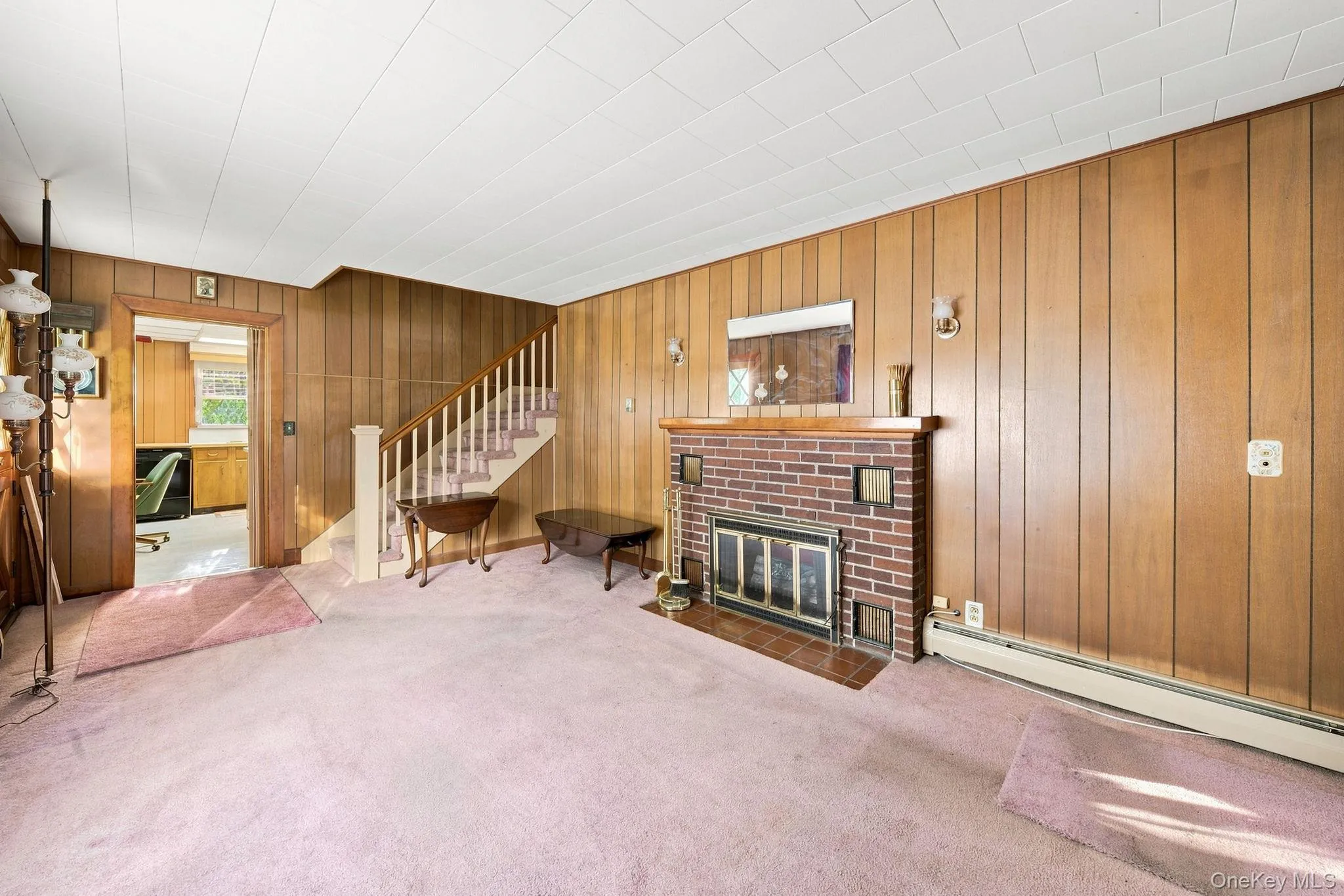Wood-paneled walls, a brick fireplace with a hearth, a staircase with white balusters, and wall-mounted sconces Wood-paneled walls, a brick fireplace with a hearth, a staircase with white balusters, and wall-mounted sconces