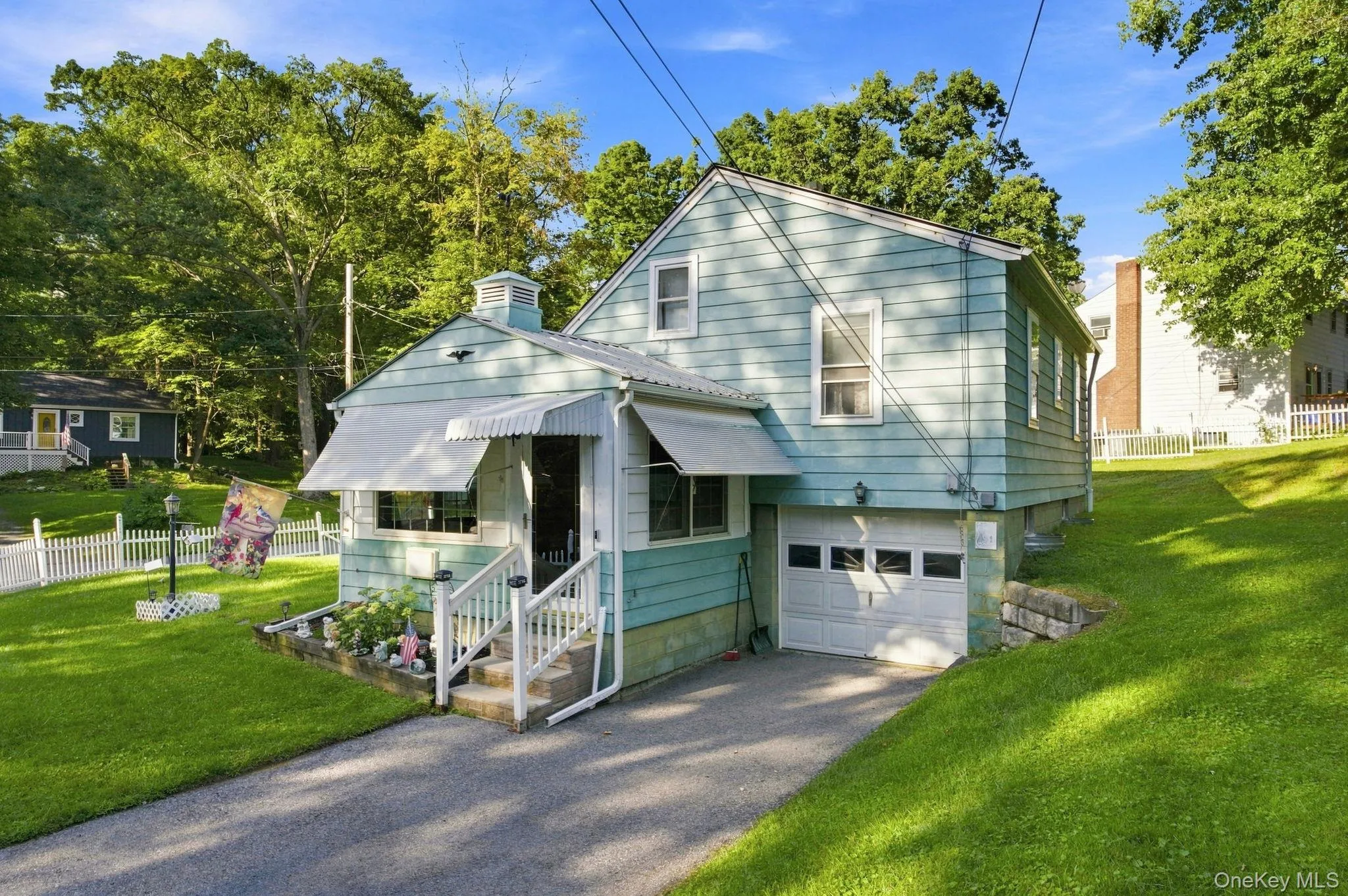 Turquoise siding exterior with a white picket fence, covered side entry, concrete steps, and an attached garage with a driveway Turquoise siding exterior with a white picket fence, covered side entry, concrete steps, and an attached garage with a driveway