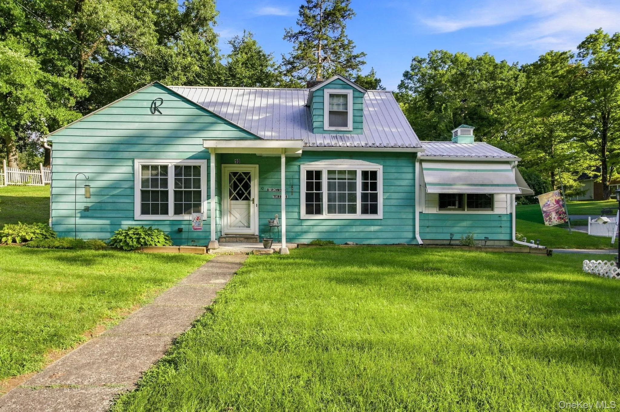 Turquoise siding exterior with white trim, metal roofing, dormer window, covered front porch, metal roof, and a concrete walkway Turquoise siding exterior with white trim, metal roofing, dormer window, covered front porch, metal roof, and a concrete walkway