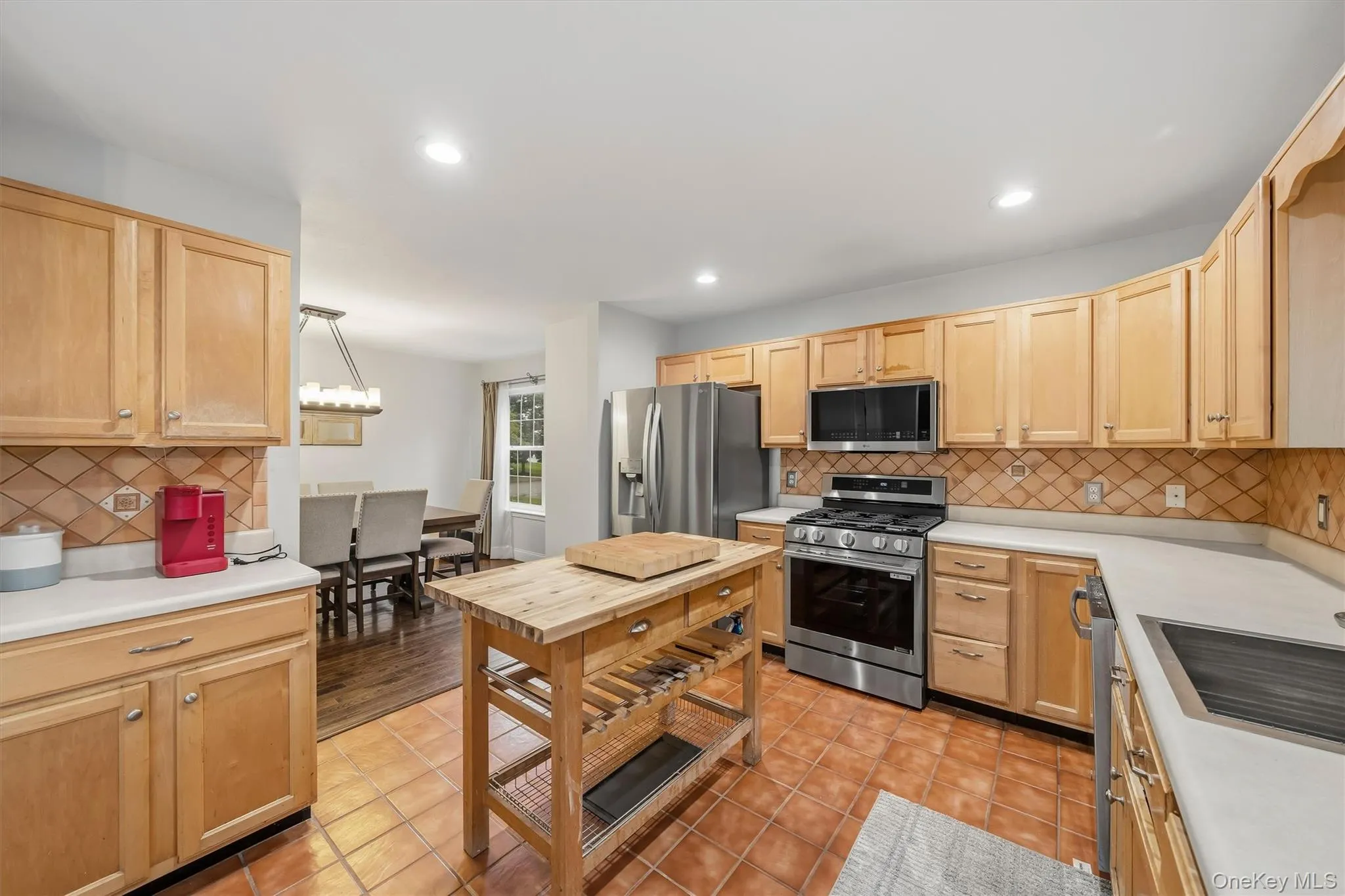 Kitchen featuring warm wood-finish cabinetry, stainless steel appliances, tiled flooring, and a portable wood-finish island Kitchen featuring warm wood-finish cabinetry, stainless steel appliances, tiled flooring, and a portable wood-finish island