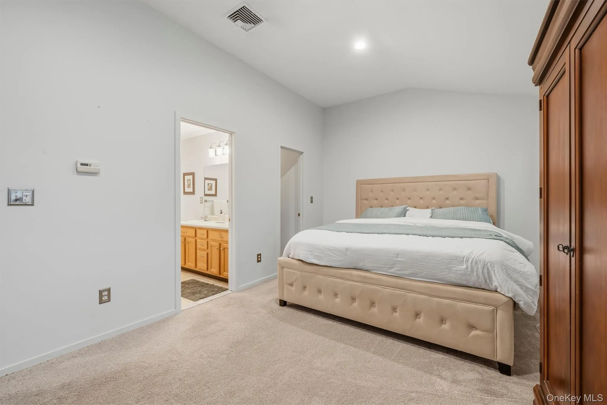 Vaulted ceiling, recessed lighting, neutral wall color, light-toned carpet, and a wooden armoire Vaulted ceiling, recessed lighting, neutral wall color, light-toned carpet, and a wooden armoire