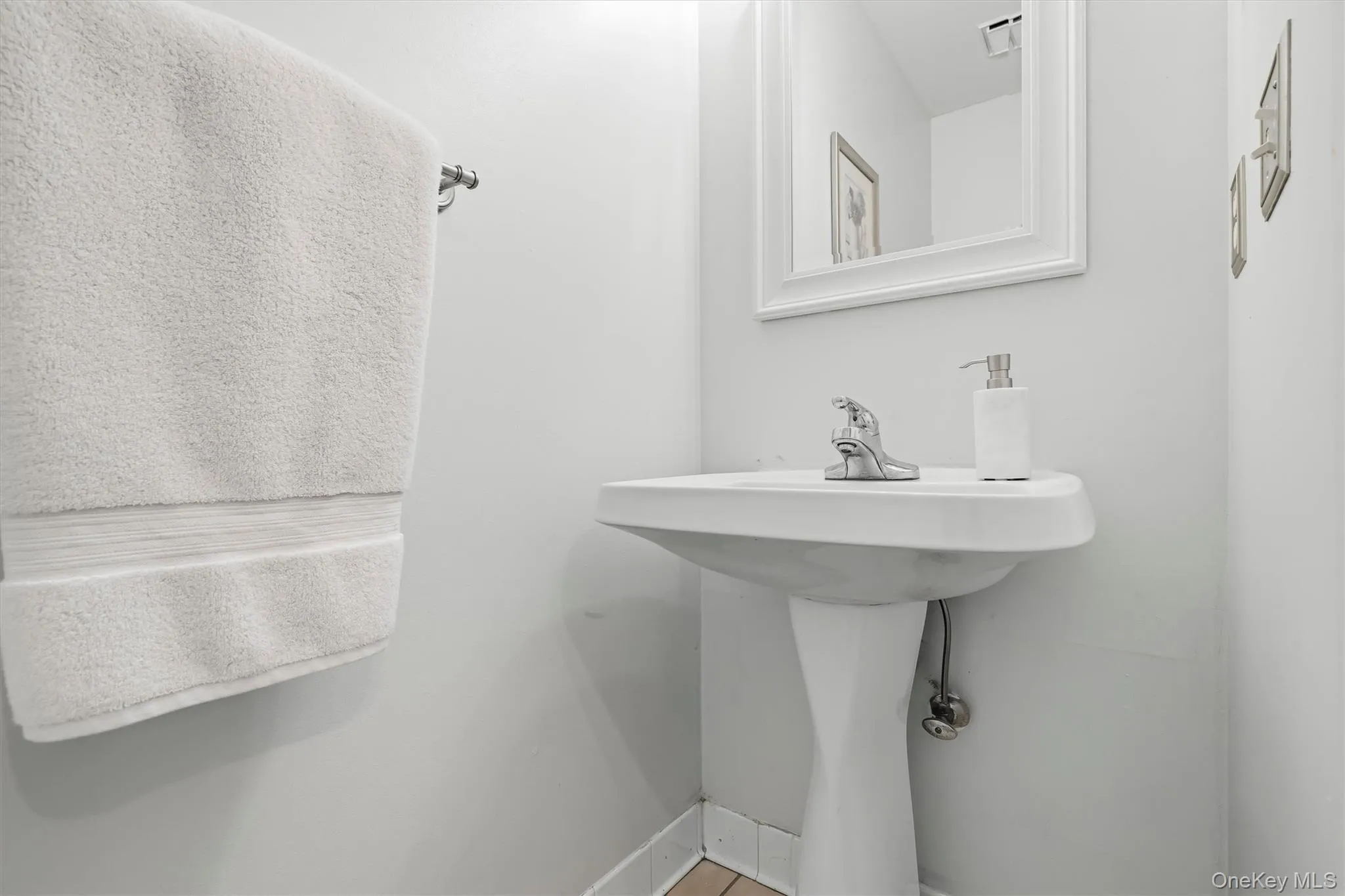 Pedestal sink with chrome faucet, complemented by a framed mirror and a towel bar Pedestal sink with chrome faucet, complemented by a framed mirror and a towel bar