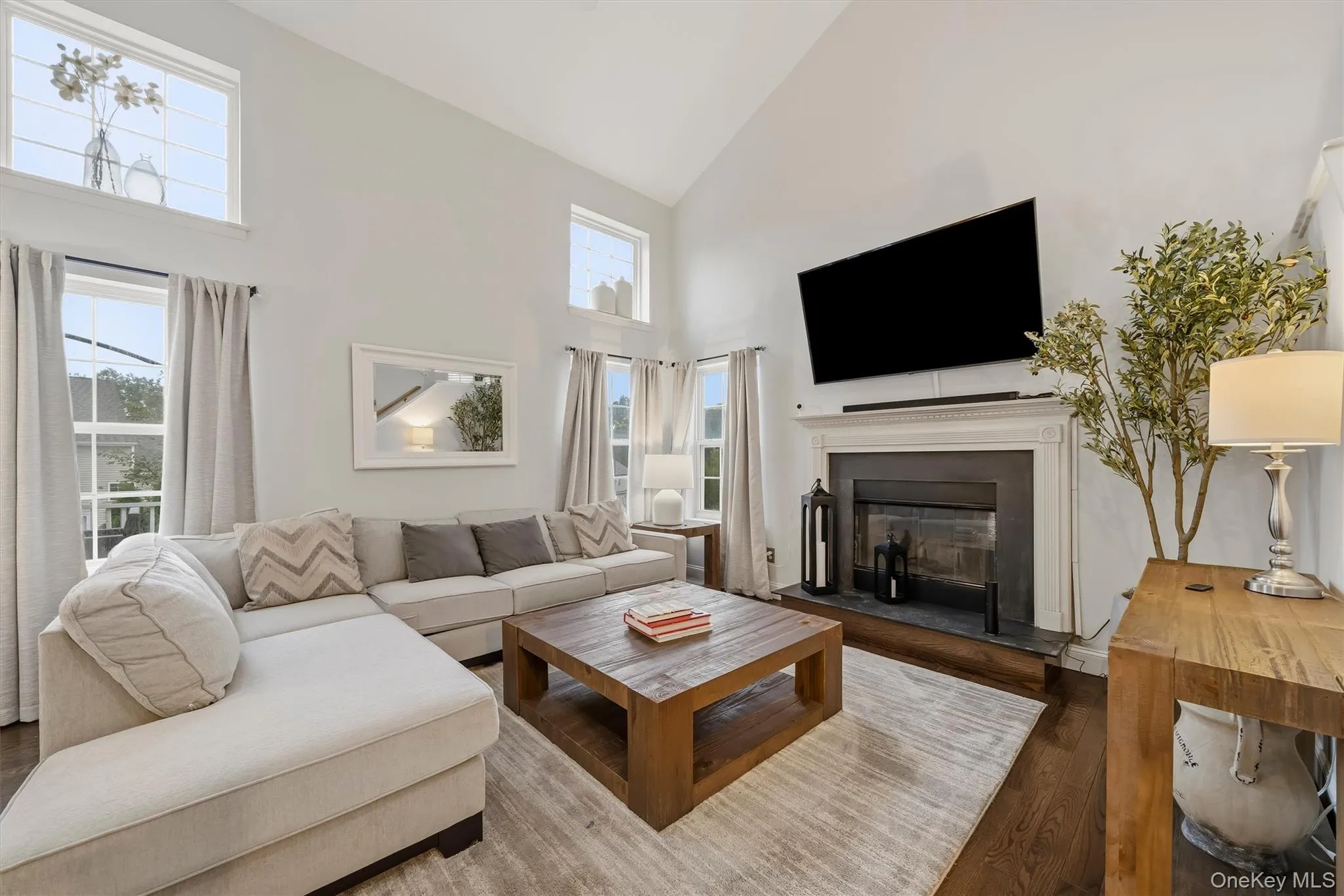 Vaulted ceiling with upper windows, fireplace with wood mantel, dark wood-finish flooring, and multiple windows Vaulted ceiling with upper windows, fireplace with wood mantel, dark wood-finish flooring, and multiple windows