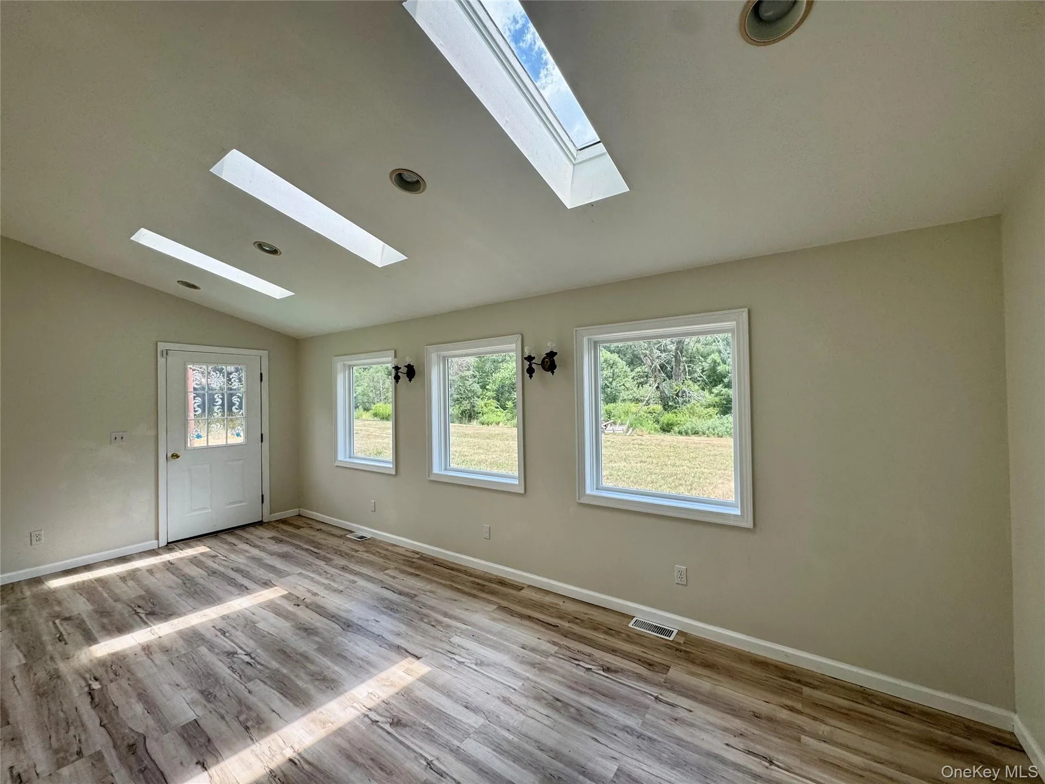 Unfinished room with a skylight, vaulted ceiling, and wood finished floors Unfinished room with a skylight, vaulted ceiling, and wood finished floors