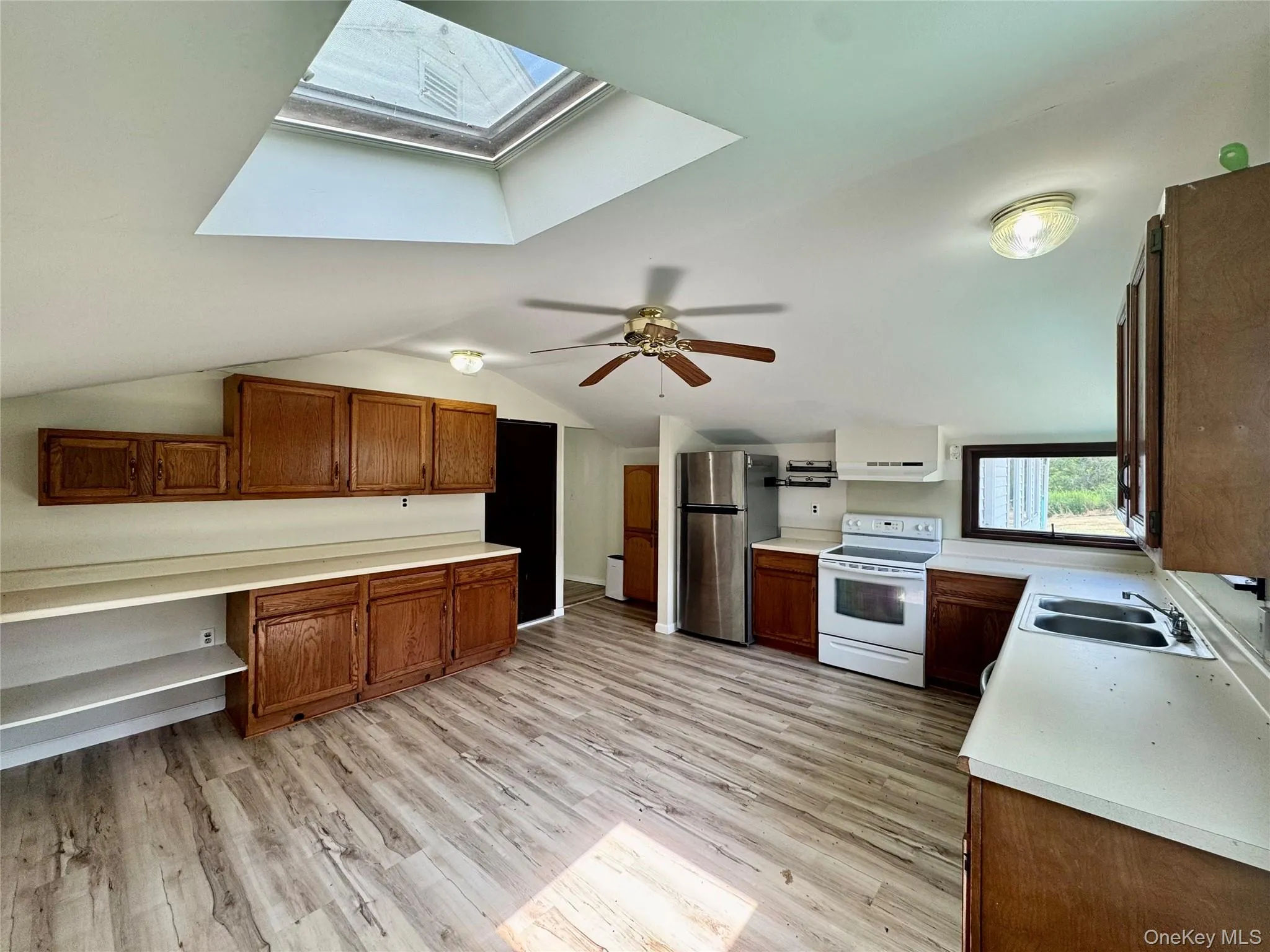 Kitchen with white electric range, a skylight, freestanding refrigerator, light wood-style floors, and brown cabinets Kitchen with white electric range, a skylight, freestanding refrigerator, light wood-style floors, and brown cabinets