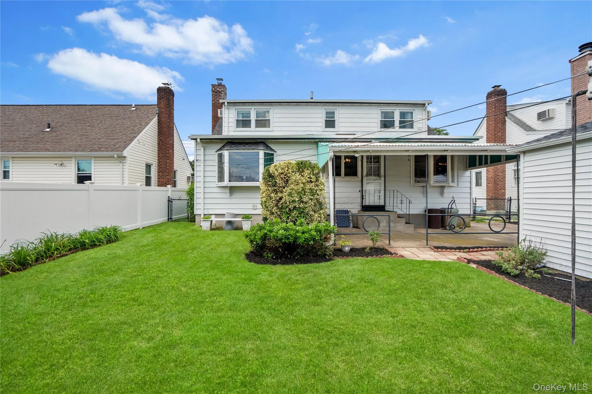 Expansive green lawn, white vinyl fencing, brick chimneys, patio with covered awning, and bay window Expansive green lawn, white vinyl fencing, brick chimneys, patio with covered awning, and bay window