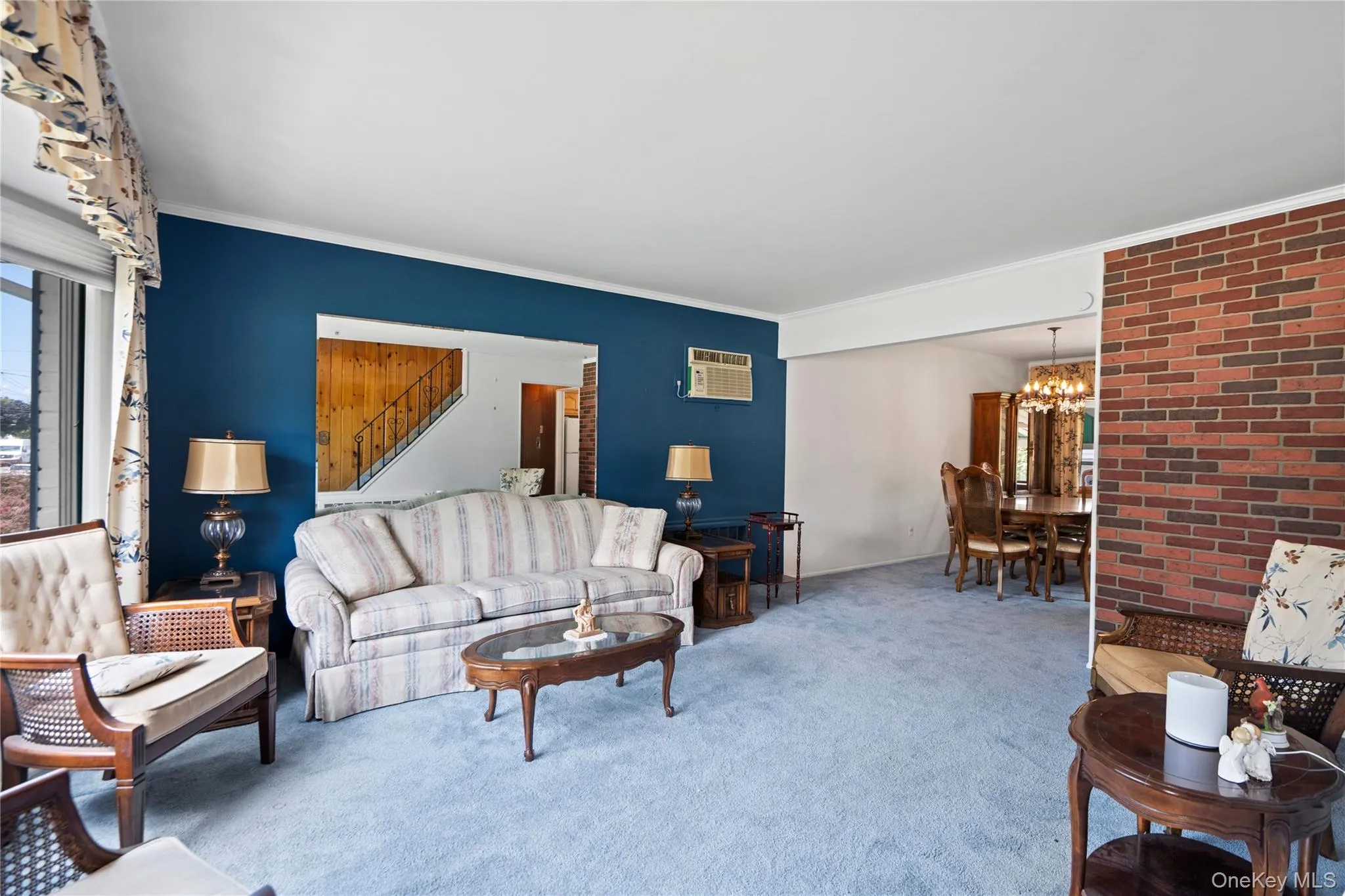 Open-concept living area with a blue accent wall, brick-finish wall, and light blue carpeting Open-concept living area with a blue accent wall, brick-finish wall, and light blue carpeting
