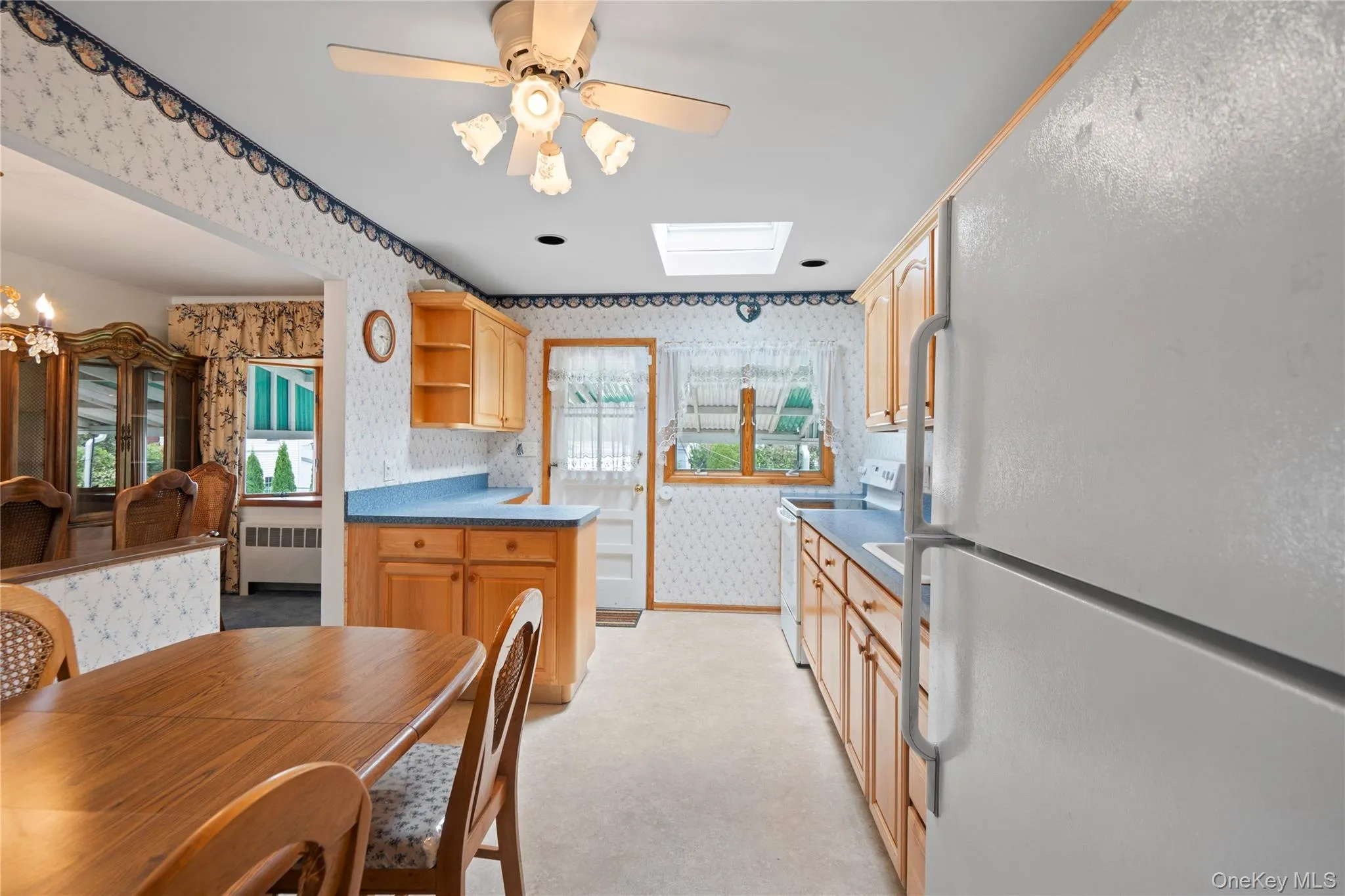 Kitchen featuring wood-finish cabinetry, white appliances, and a skylight Kitchen featuring wood-finish cabinetry, white appliances, and a skylight