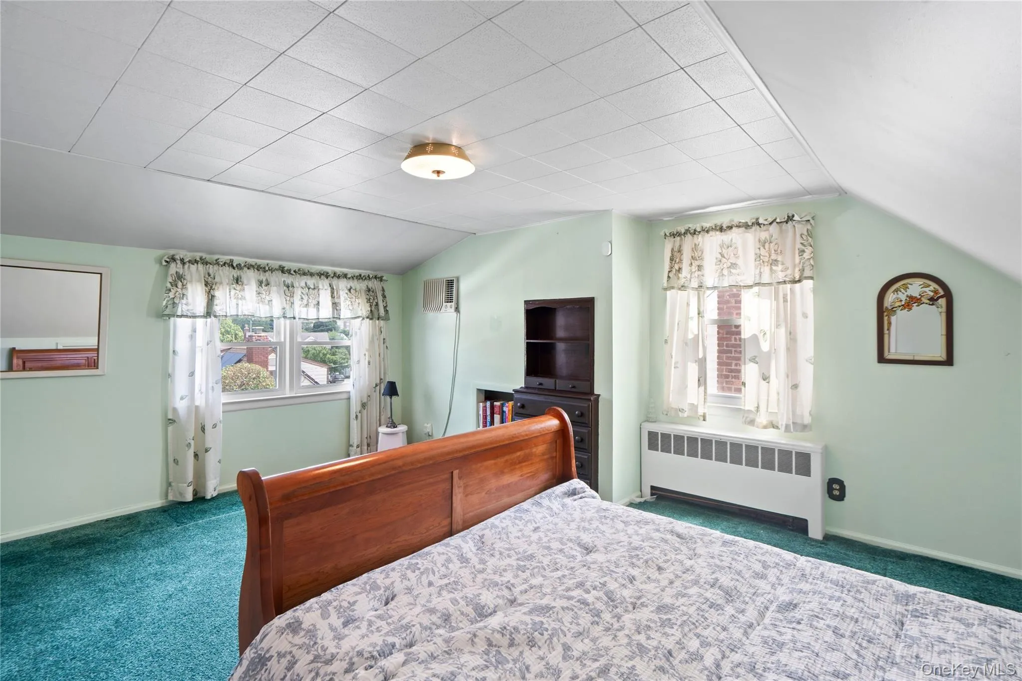 Ceiling tiles, wall-mounted light fixture, window with drapes, and green carpeting Ceiling tiles, wall-mounted light fixture, window with drapes, and green carpeting