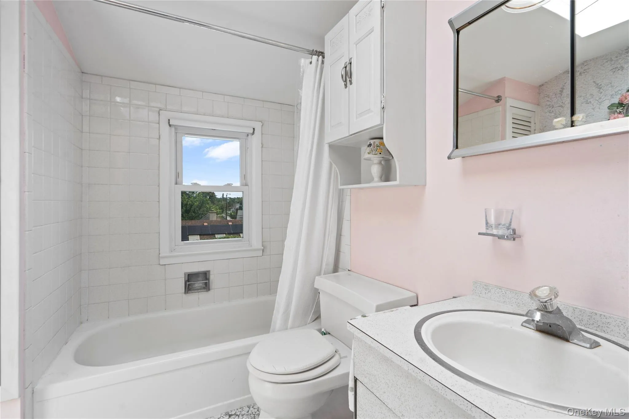 White tiled tub surround with a window, white vanity with integrated sink, and wall-mounted medicine cabinet with mirror White tiled tub surround with a window, white vanity with integrated sink, and wall-mounted medicine cabinet with mirror