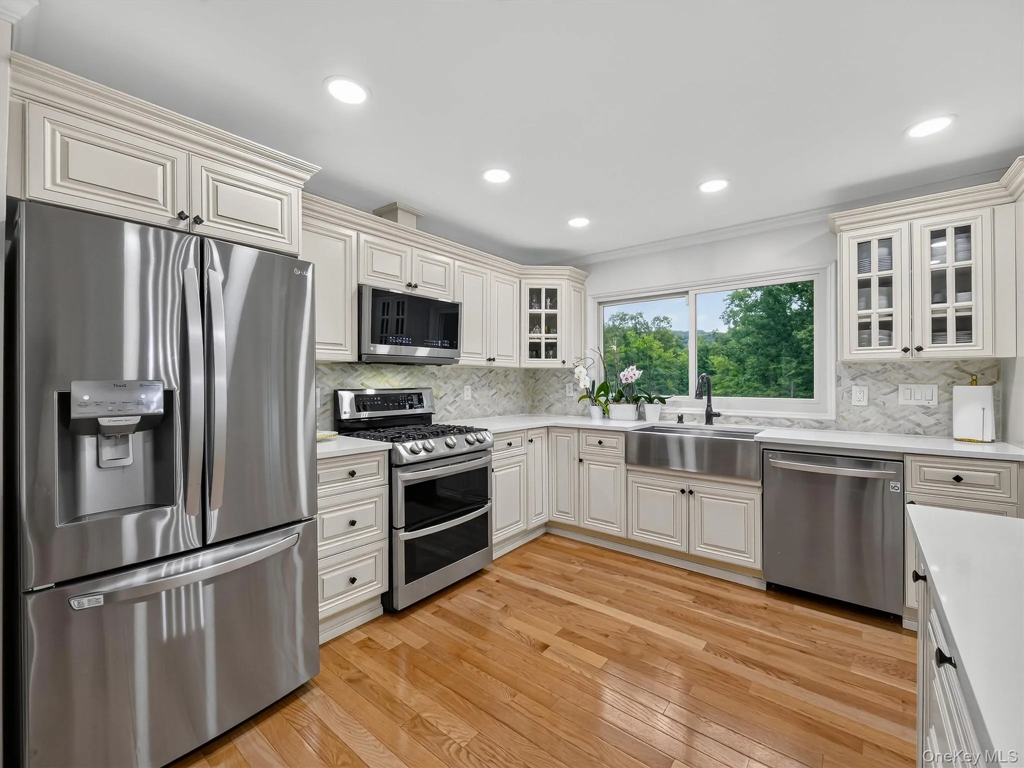 Kitchen featuring wood-finish flooring, white cabinetry, stainless steel appliances, white countertops, and a tile backsplash Kitchen featuring wood-finish flooring, white cabinetry, stainless steel appliances, white countertops, and a tile backsplash