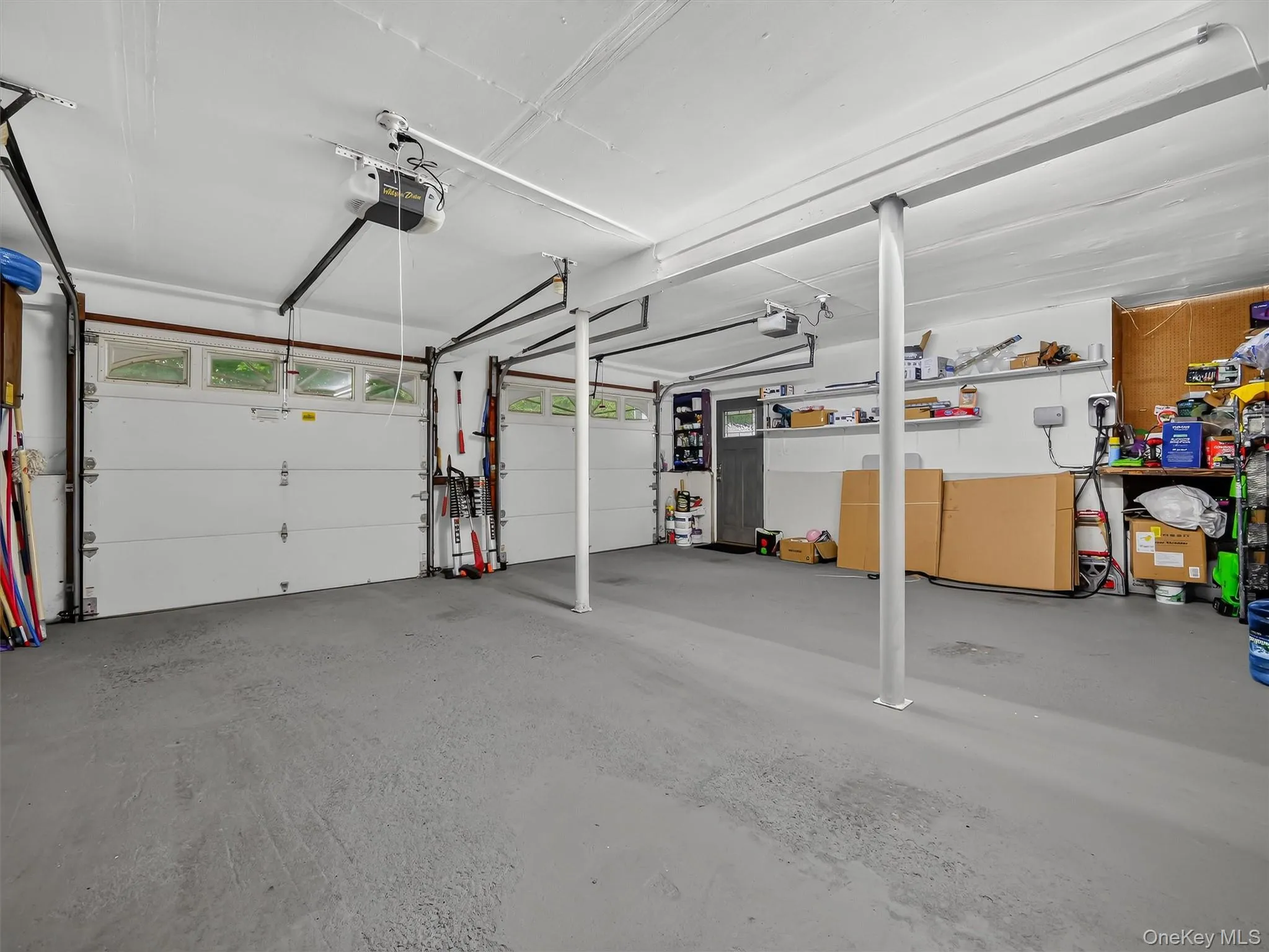 Two overhead garage doors with frosted transom windows, painted concrete flooring, and a dedicated EV charging station Two overhead garage doors with frosted transom windows, painted concrete flooring, and a dedicated EV charging station