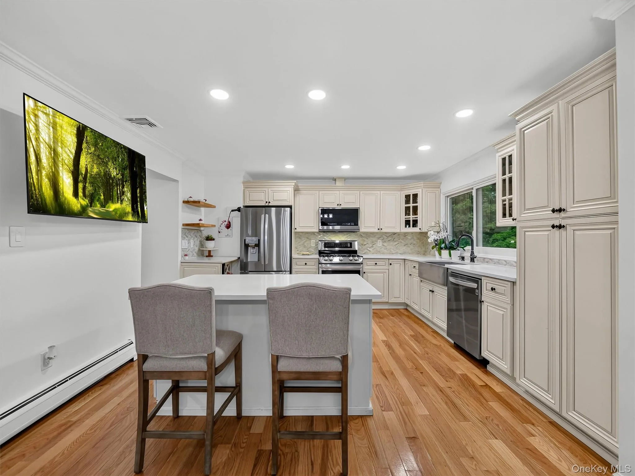 Kitchen featuring wood-finish flooring, recessed lighting, a central island with a white countertop, extensive cabinetry, and stainless steel appliances Kitchen featuring wood-finish flooring, recessed lighting, a central island with a white countertop, extensive cabinetry, and stainless steel appliances
