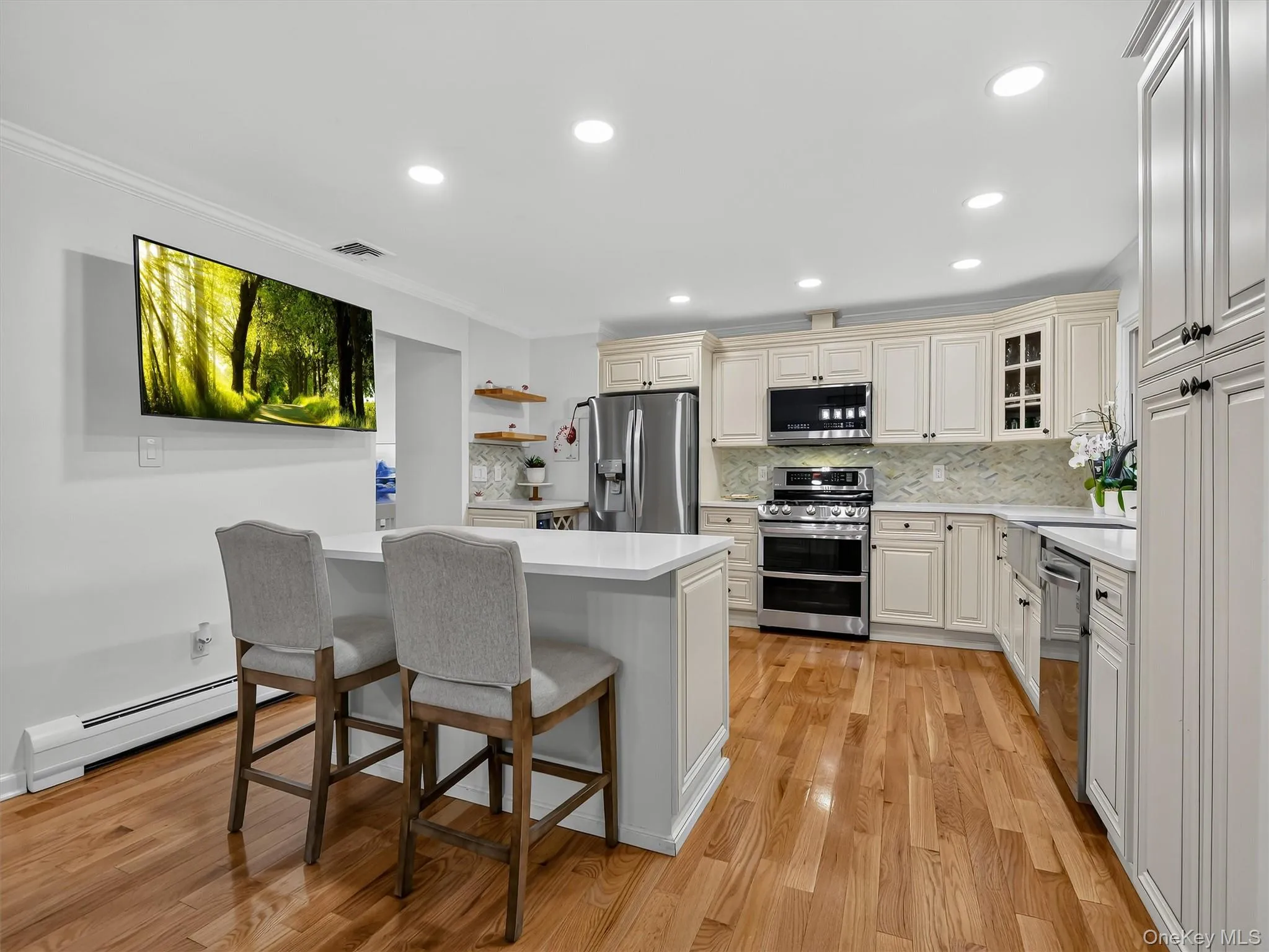 Kitchen featuring wood-finish flooring, recessed lighting, white cabinetry, stainless steel appliances, and a central island with a countertop Kitchen featuring wood-finish flooring, recessed lighting, white cabinetry, stainless steel appliances, and a central island with a countertop