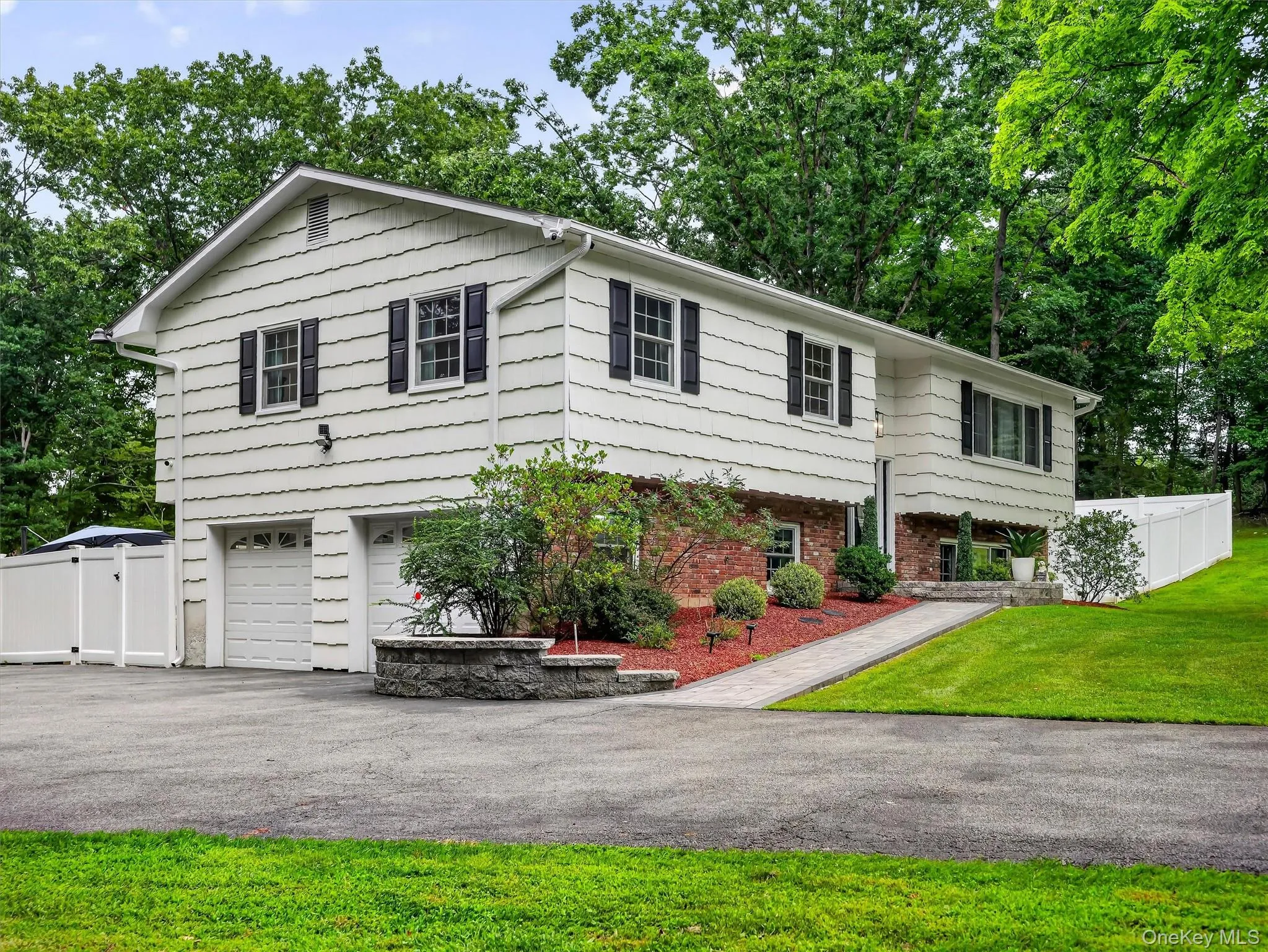 Split-level residence featuring white siding, black window shutters, and a two-car garage Split-level residence featuring white siding, black window shutters, and a two-car garage