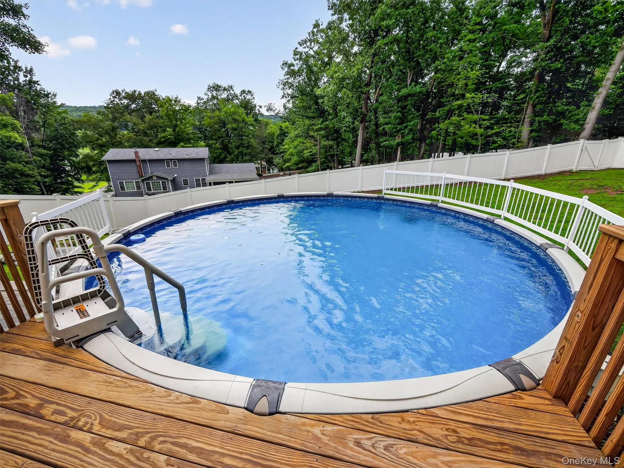 Above-ground pool with a surrounding wood deck, white privacy fencing, and an integrated pool ladder Above-ground pool with a surrounding wood deck, white privacy fencing, and an integrated pool ladder