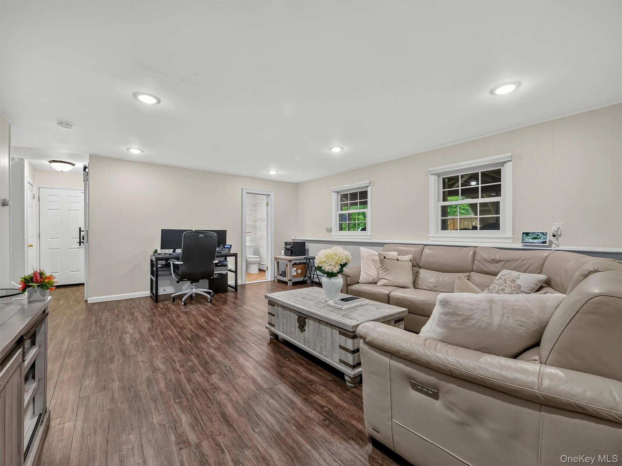 Recessed ceiling lighting, wood-finish flooring, two windows with white trim, and a three-panel interior door Recessed ceiling lighting, wood-finish flooring, two windows with white trim, and a three-panel interior door