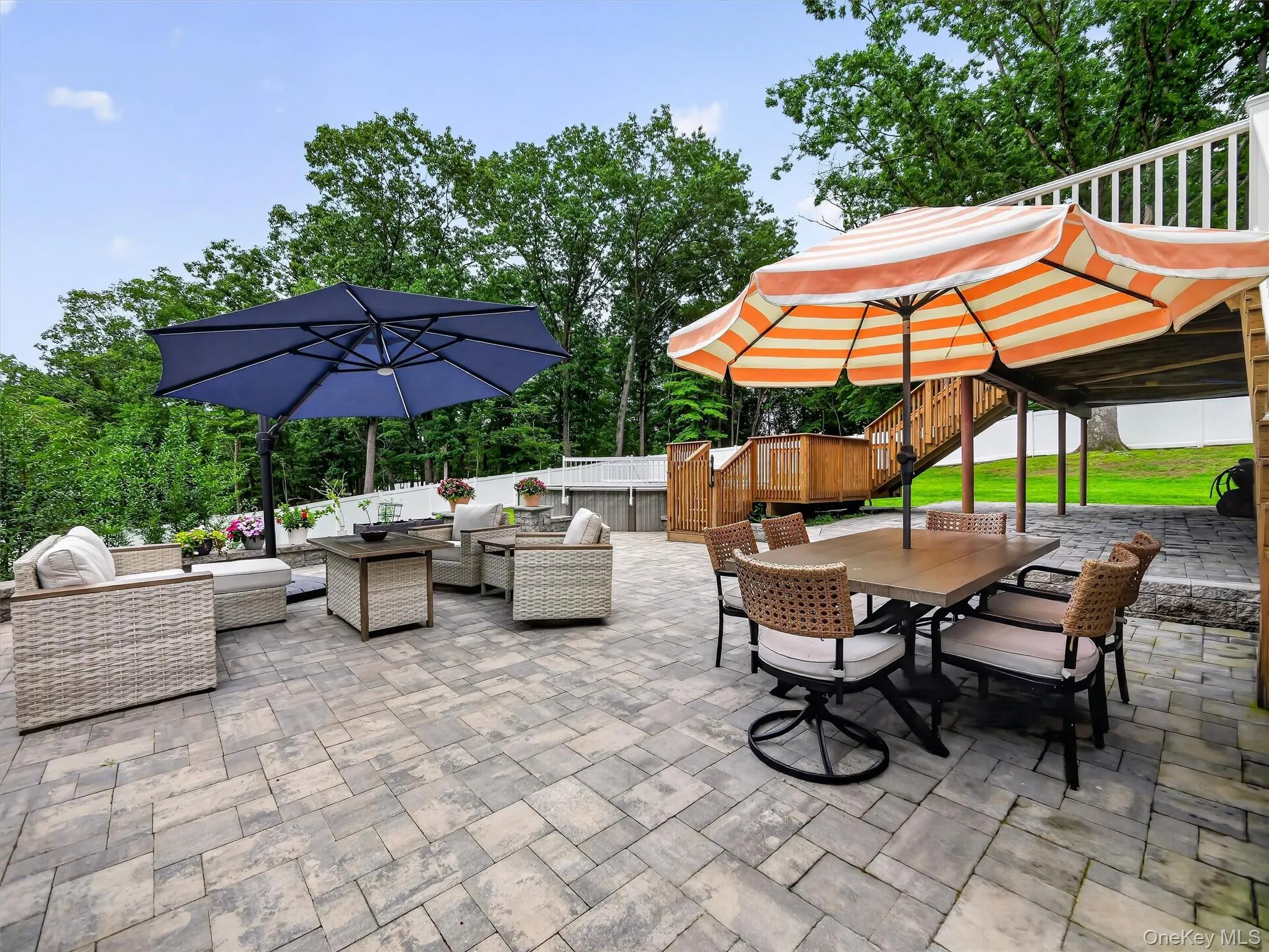 Expansive paver patio with a multi-level deck featuring a wooden privacy fence and white railings Expansive paver patio with a multi-level deck featuring a wooden privacy fence and white railings