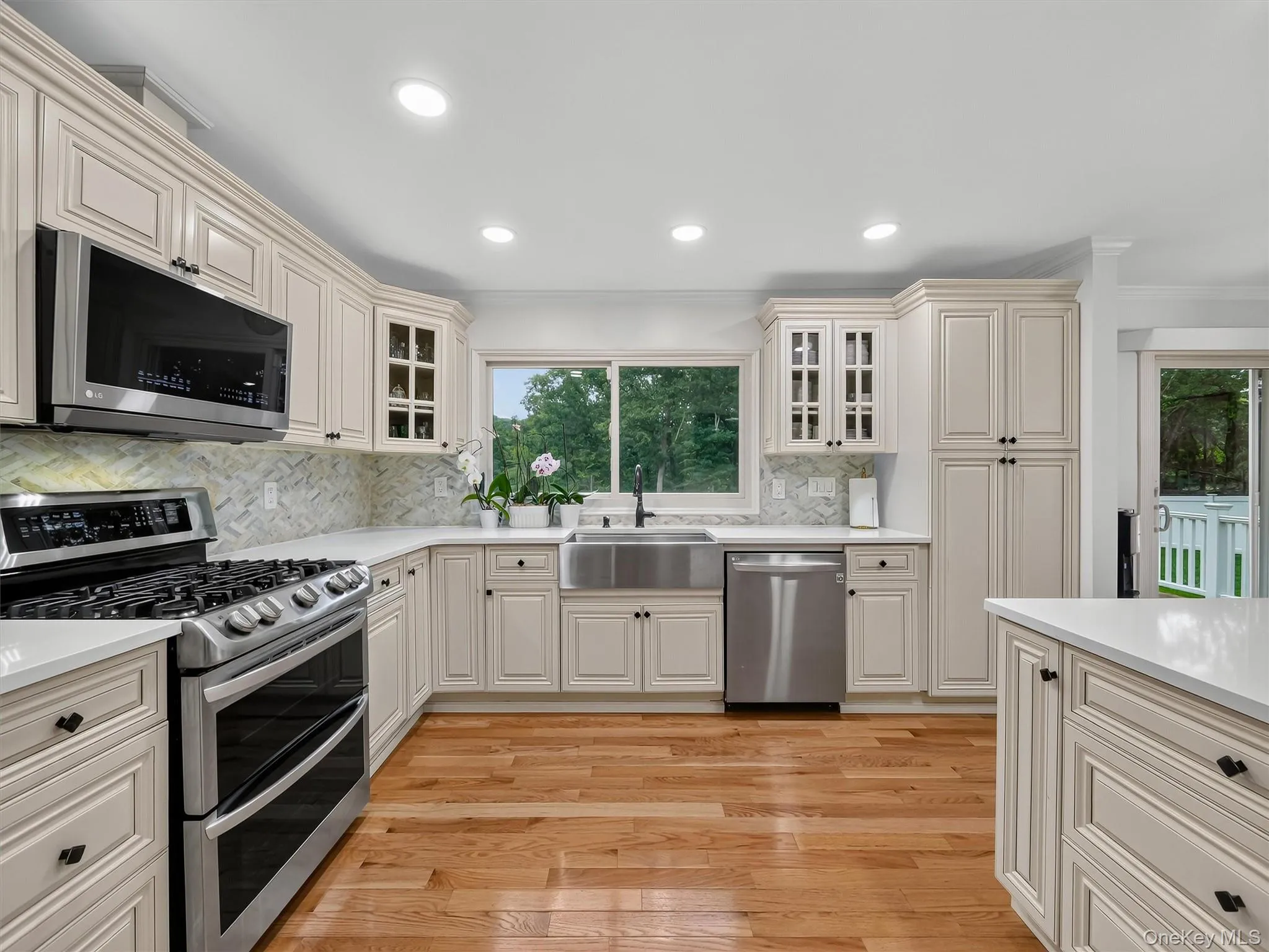 Recessed lighting, wood-finish flooring, light-toned cabinetry, stainless steel appliances, and a tile backsplash Recessed lighting, wood-finish flooring, light-toned cabinetry, stainless steel appliances, and a tile backsplash