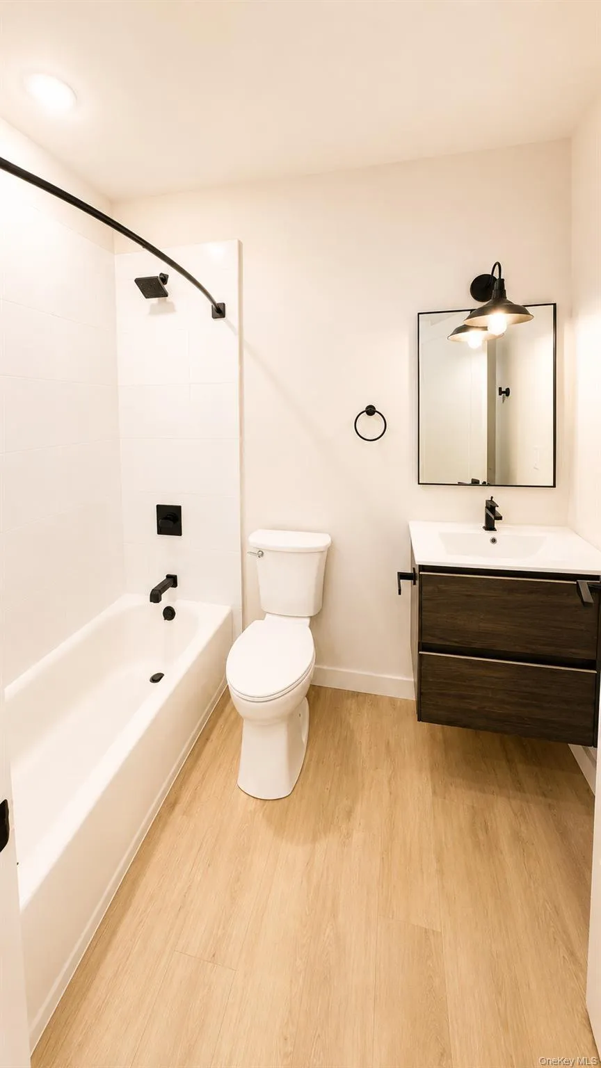 Light wood-finish flooring, floating dark wood-finish vanity, integrated sink, and black fixtures Light wood-finish flooring, floating dark wood-finish vanity, integrated sink, and black fixtures