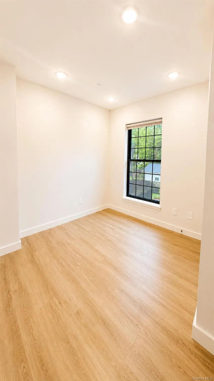 Recessed lighting, wood-finish flooring, and a single window with black framing Recessed lighting, wood-finish flooring, and a single window with black framing