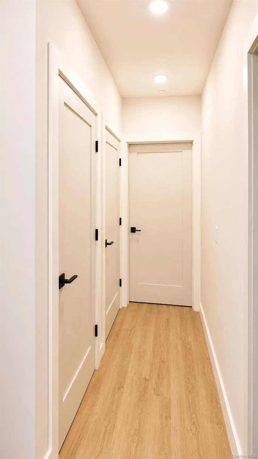 Wood-finish flooring, recessed lighting, matte black door hardware, white trim, and white paneled doors Wood-finish flooring, recessed lighting, matte black door hardware, white trim, and white paneled doors