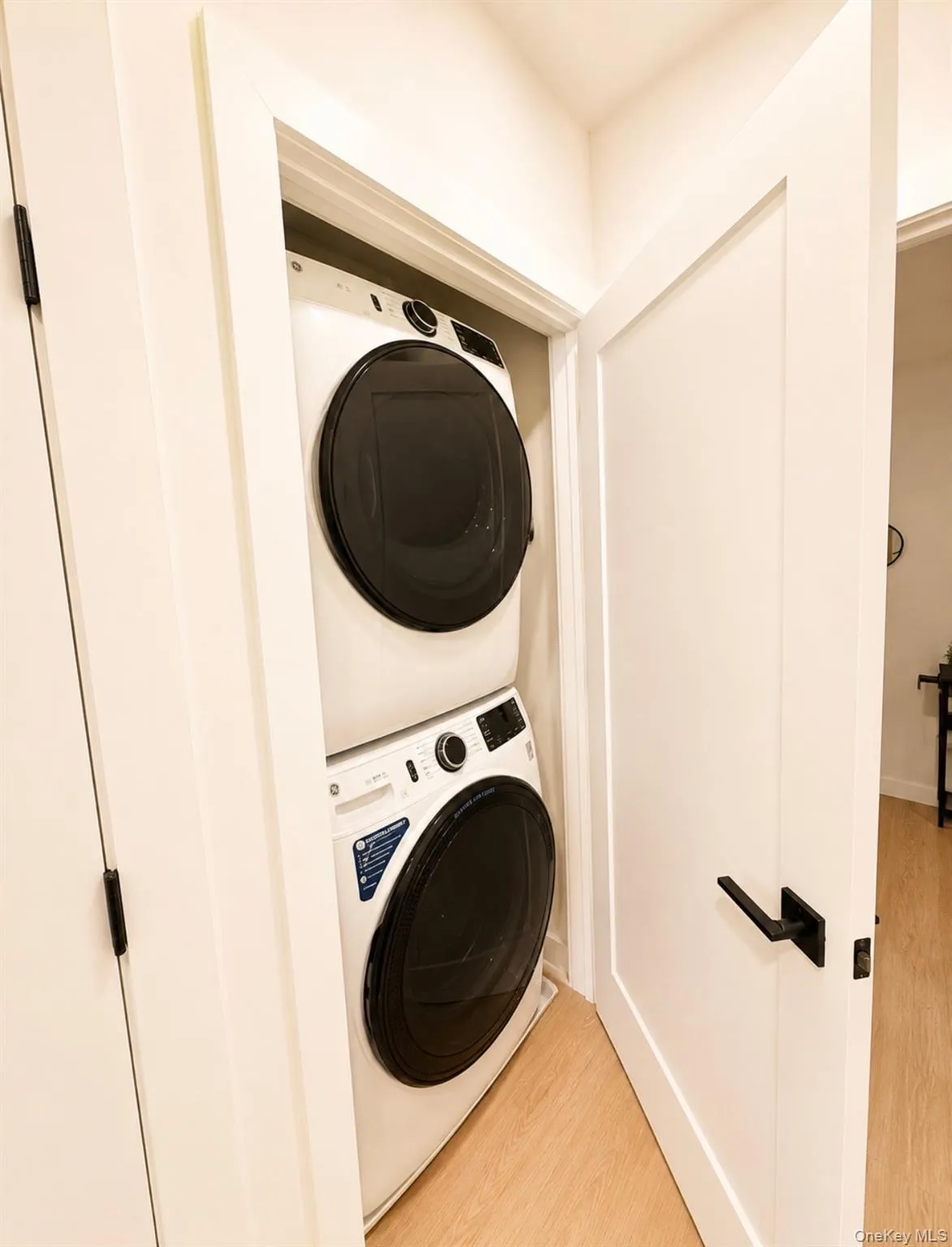 Stackable washer and dryer within a dedicated closet, featuring a light wood-finish flooring and contemporary black hardware on the door Stackable washer and dryer within a dedicated closet, featuring a light wood-finish flooring and contemporary black hardware on the door