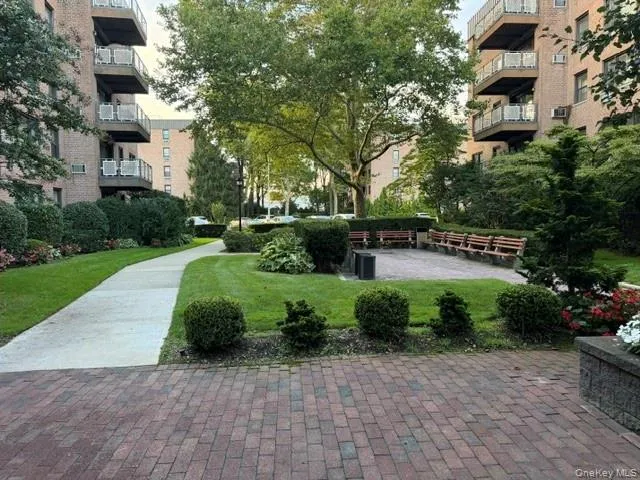 Landscaped courtyard featuring a paver patio, winding concrete pathway, mature trees, and shrubs Landscaped courtyard featuring a paver patio, winding concrete pathway, mature trees, and shrubs
