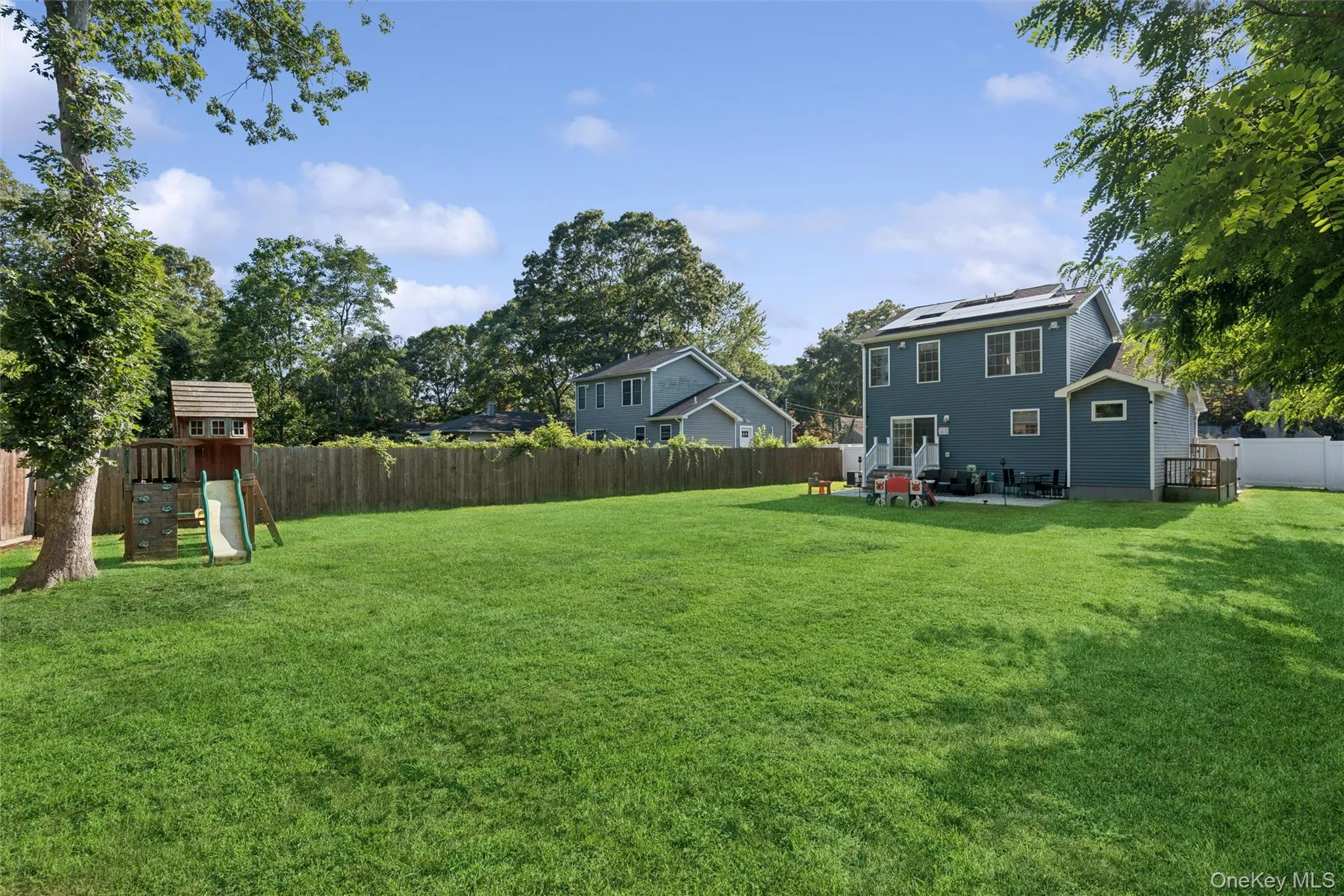 Expansive backyard featuring a manicured lawn, wood fencing, and a two-story residence with dark siding Expansive backyard featuring a manicured lawn, wood fencing, and a two-story residence with dark siding