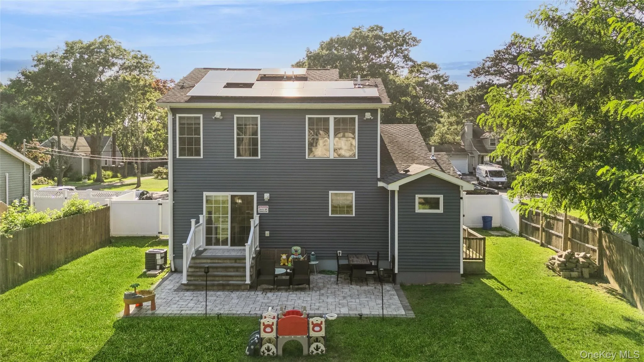 Expansive backyard featuring a manicured lawn, paver patio, sliding glass door, and solar panels Expansive backyard featuring a manicured lawn, paver patio, sliding glass door, and solar panels
