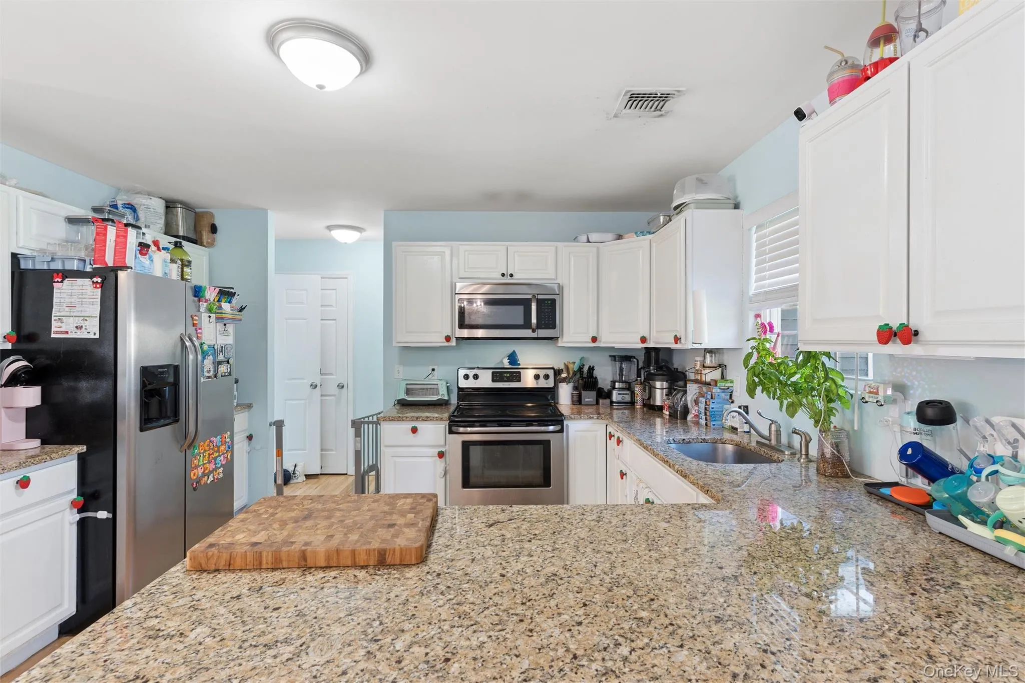 Kitchen featuring granite countertops, white cabinetry, stainless steel appliances, and a window with blinds Kitchen featuring granite countertops, white cabinetry, stainless steel appliances, and a window with blinds