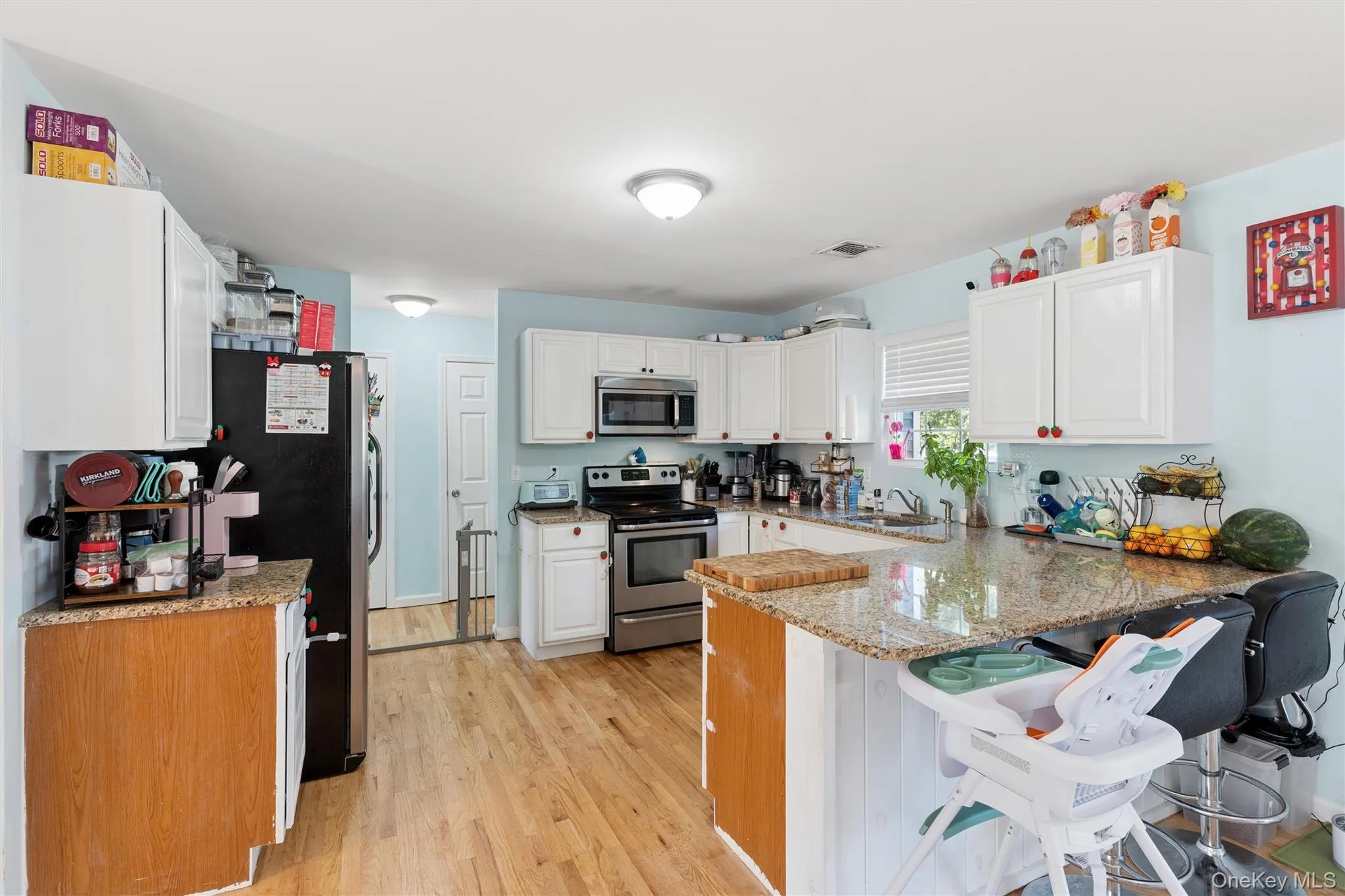 Kitchen featuring wood-finish flooring, white cabinetry, integrated stainless steel appliances, and a breakfast bar with stone countertops Kitchen featuring wood-finish flooring, white cabinetry, integrated stainless steel appliances, and a breakfast bar with stone countertops