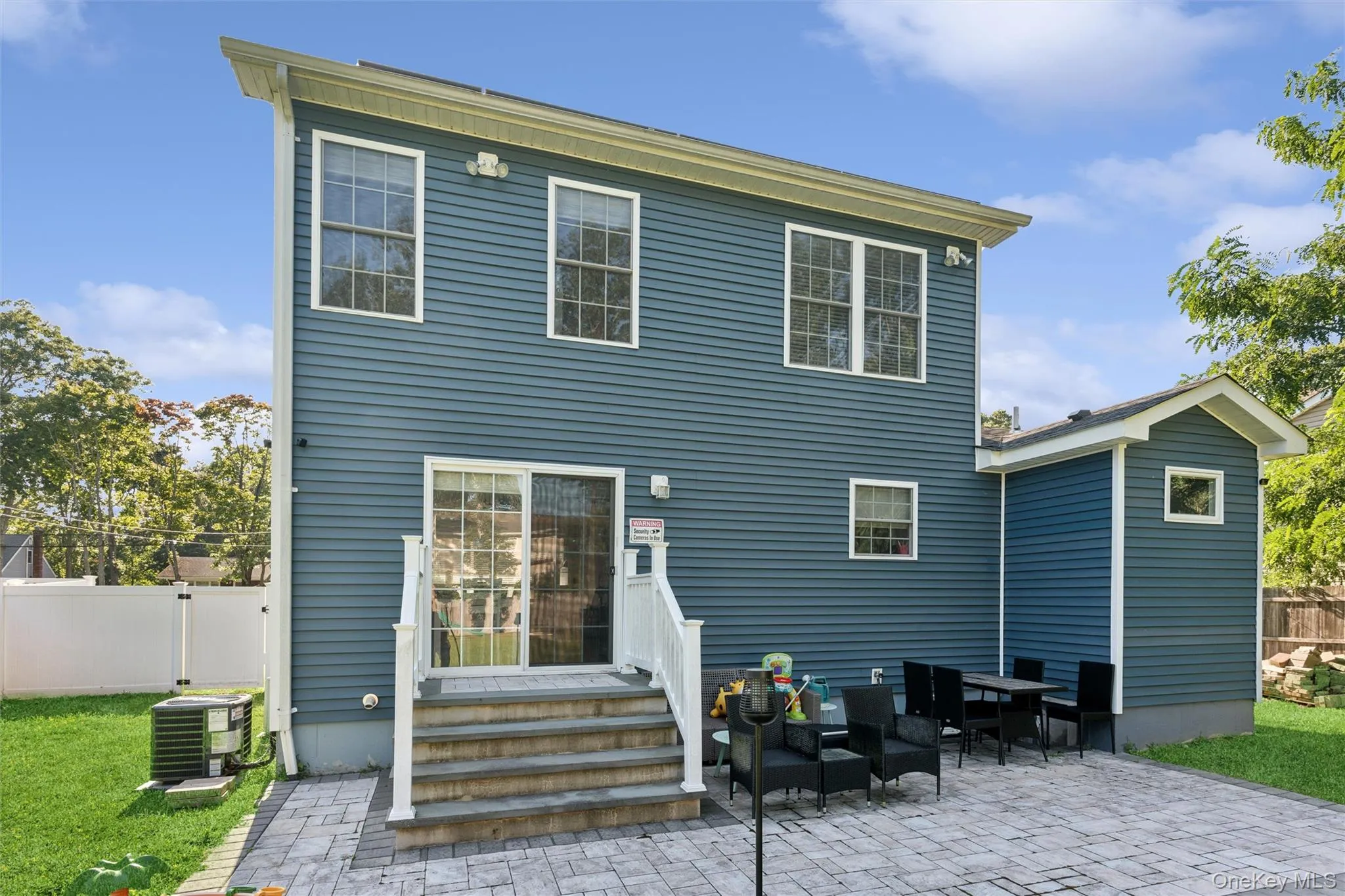 Rear elevation featuring blue siding, a ground-level paver patio, a sliding glass door, and a white privacy fence Rear elevation featuring blue siding, a ground-level paver patio, a sliding glass door, and a white privacy fence