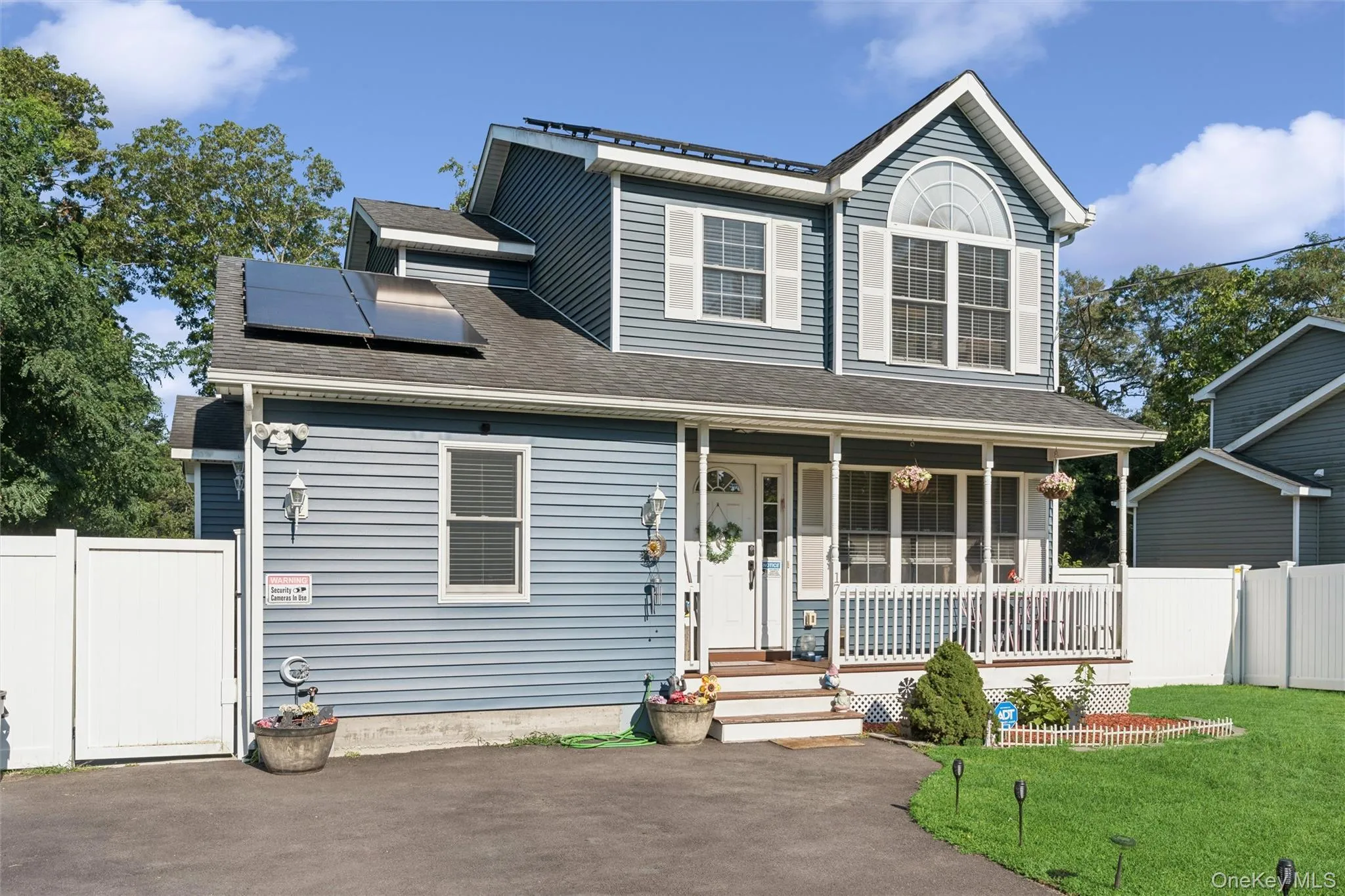 Two-story residence featuring siding exterior, an arched window, a covered front porch, and solar panels Two-story residence featuring siding exterior, an arched window, a covered front porch, and solar panels