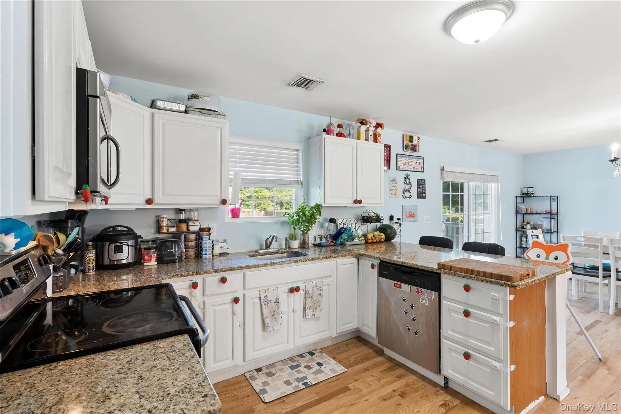 Kitchen featuring wood-finish flooring, white cabinetry, granite countertops, and stainless steel appliances Kitchen featuring wood-finish flooring, white cabinetry, granite countertops, and stainless steel appliances