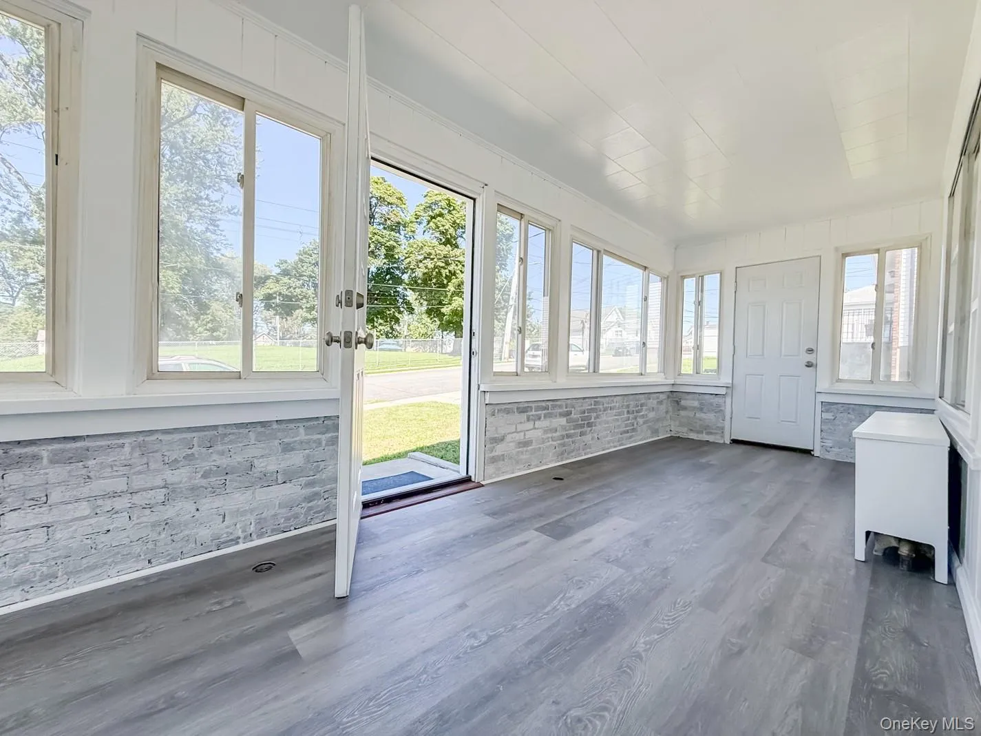 Sun-drenched room featuring extensive window placement, wood-finish flooring, white painted brick wall accents, and a white panel door Sun-drenched room featuring extensive window placement, wood-finish flooring, white painted brick wall accents, and a white panel door