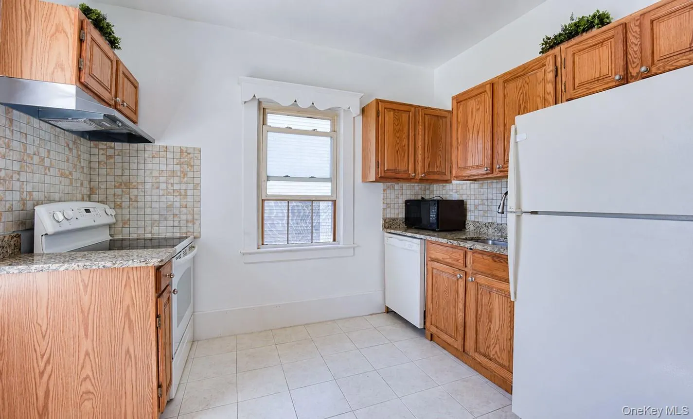 Kitchen featuring wood cabinetry, light-toned tile flooring, granite-style countertops, and a tile backsplash Kitchen featuring wood cabinetry, light-toned tile flooring, granite-style countertops, and a tile backsplash