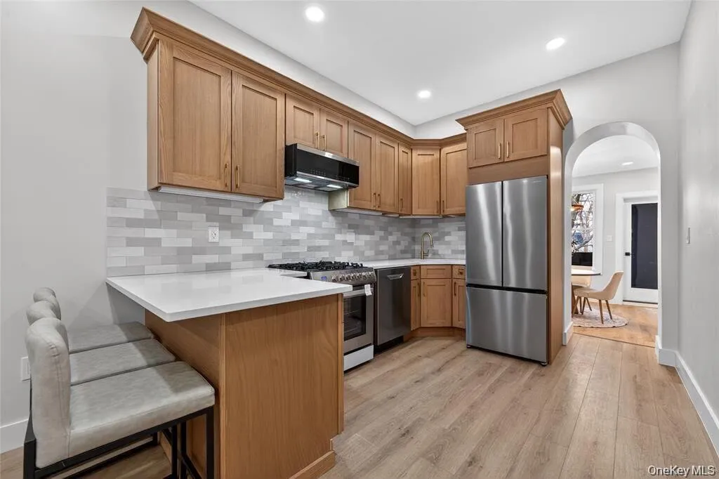 Kitchen with wood-finish flooring, light-toned cabinetry, light-colored countertops, stainless steel appliances, and a tiled backsplash Kitchen with wood-finish flooring, light-toned cabinetry, light-colored countertops, stainless steel appliances, and a tiled backsplash