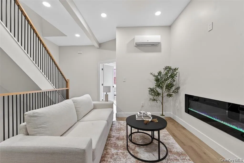 Recessed ceiling lighting, wood-finish flooring, staircase with metal balusters, wall-mounted air conditioning unit, and a built-in electric fireplace Recessed ceiling lighting, wood-finish flooring, staircase with metal balusters, wall-mounted air conditioning unit, and a built-in electric fireplace
