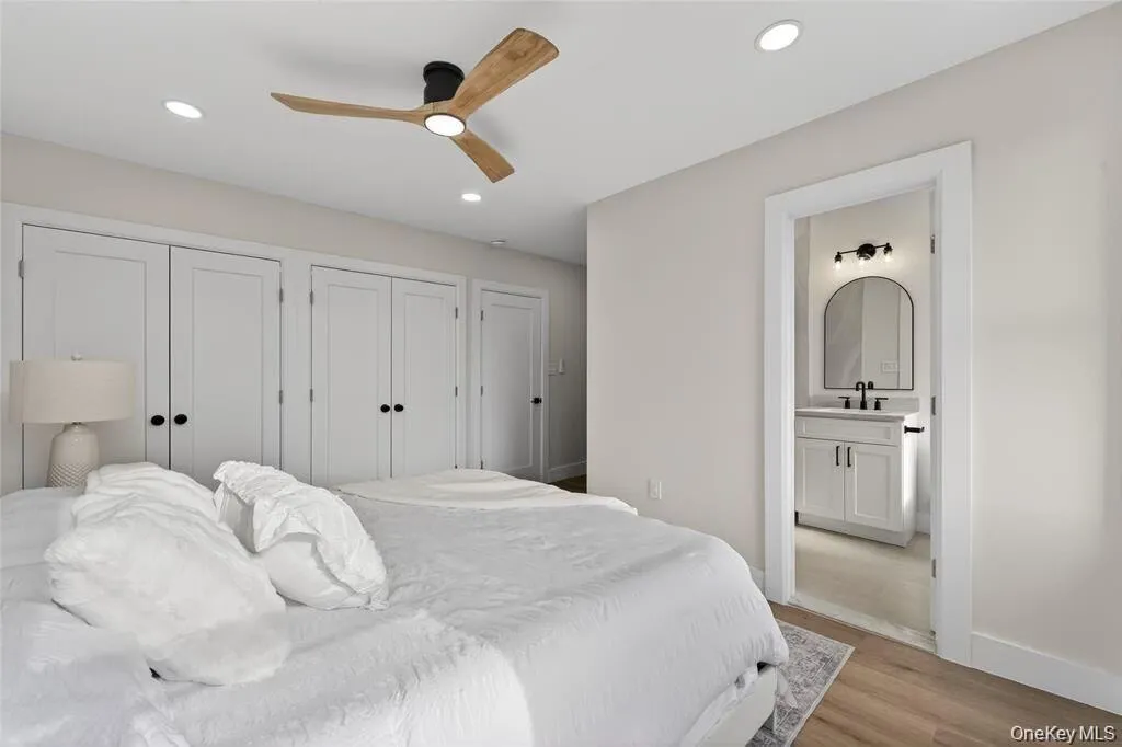 Recessed lighting, wood-finish flooring, contemporary ceiling fan, multiple panel doors, and a bathroom with an arched mirror and single vanity Recessed lighting, wood-finish flooring, contemporary ceiling fan, multiple panel doors, and a bathroom with an arched mirror and single vanity