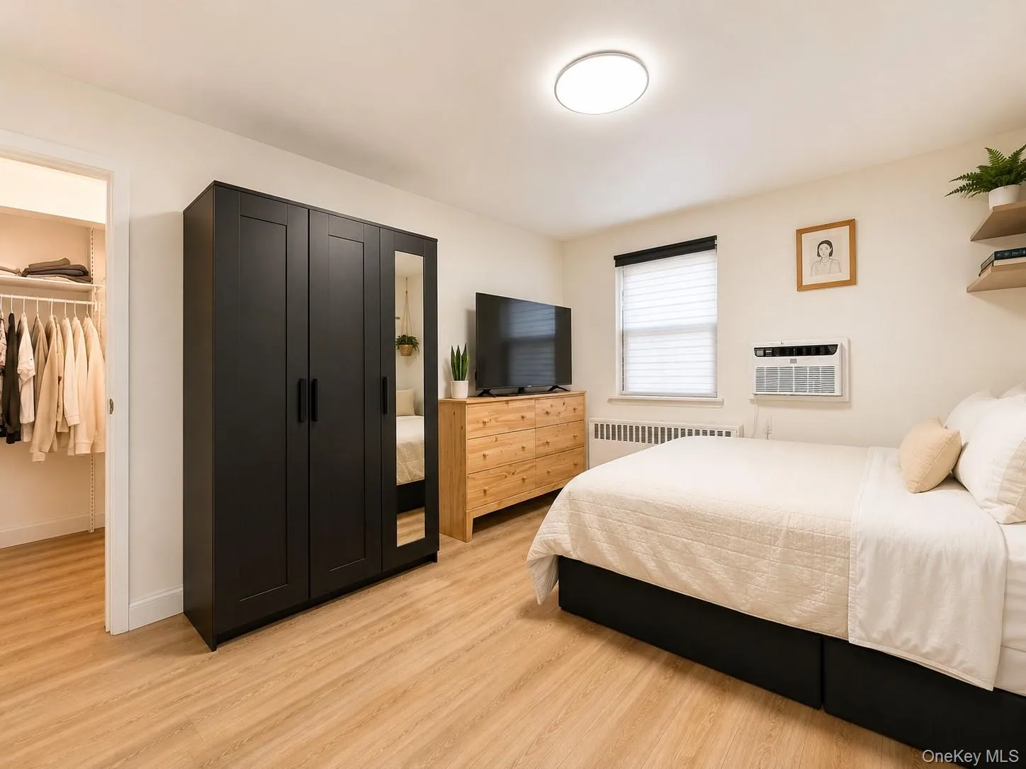 Light wood-finish flooring, walk-in closet with wire shelving, window with blinds, wall-mounted air conditioning unit, and flush-mount ceiling light Light wood-finish flooring, walk-in closet with wire shelving, window with blinds, wall-mounted air conditioning unit, and flush-mount ceiling light
