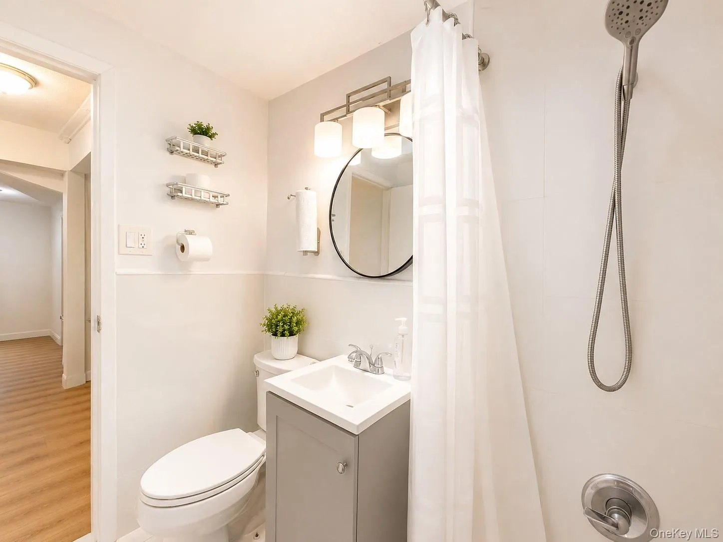 Bathroom featuring a modern vanity with a white countertop, wall-mounted light fixture, and a tiled shower surround with an adjustable showerhead Bathroom featuring a modern vanity with a white countertop, wall-mounted light fixture, and a tiled shower surround with an adjustable showerhead