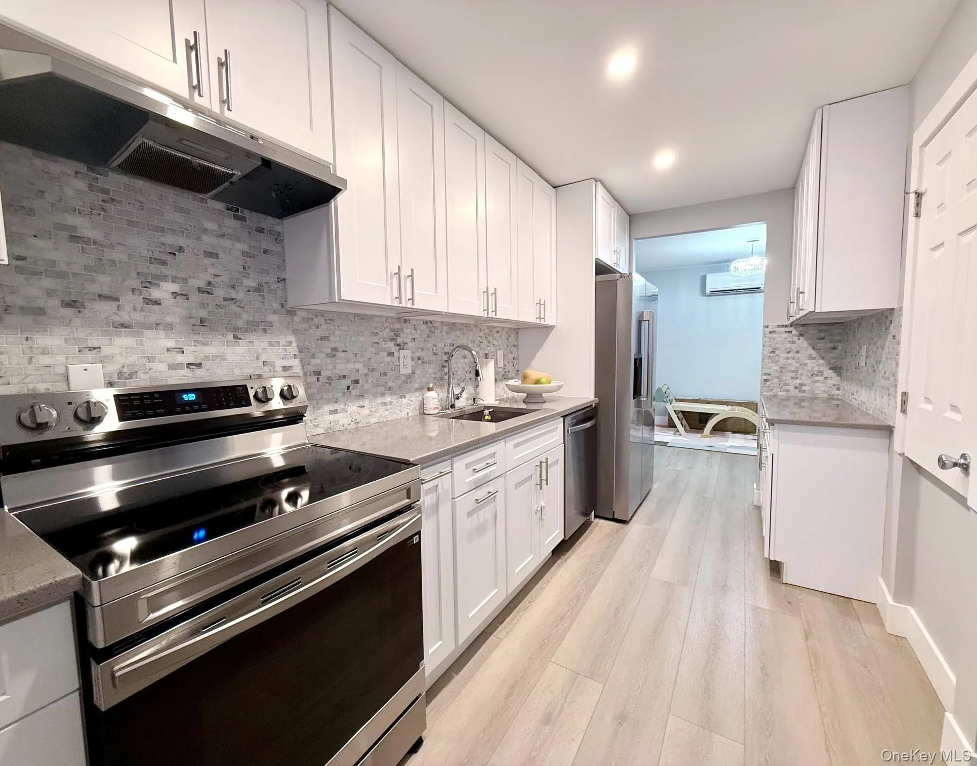 White shaker cabinetry, light wood-finish flooring, stainless steel appliances, stone countertops, and a full tile backsplash White shaker cabinetry, light wood-finish flooring, stainless steel appliances, stone countertops, and a full tile backsplash