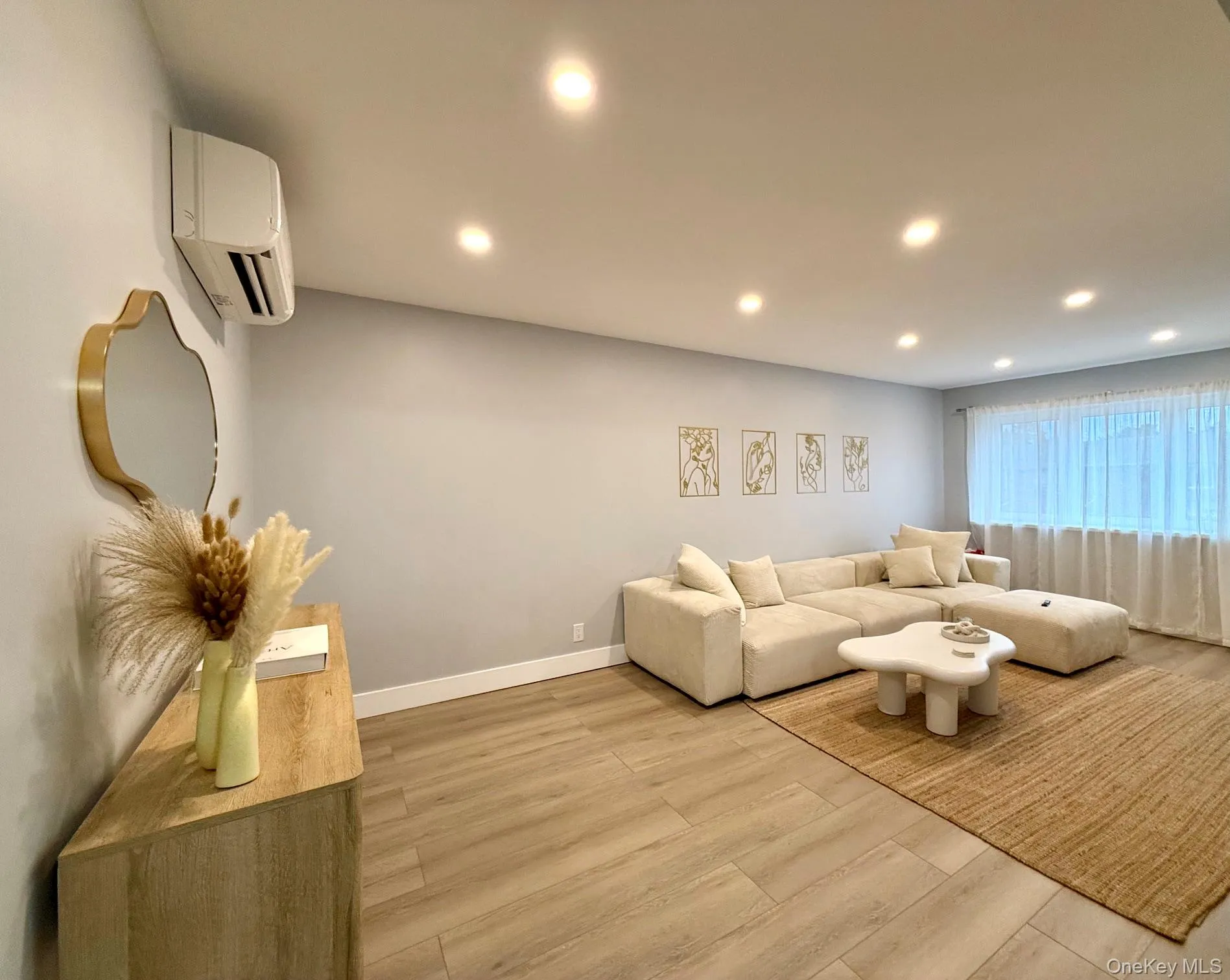 Recessed ceiling lighting, wood-finish flooring, light wall coloration, and a window with sheer full-length coverings Recessed ceiling lighting, wood-finish flooring, light wall coloration, and a window with sheer full-length coverings