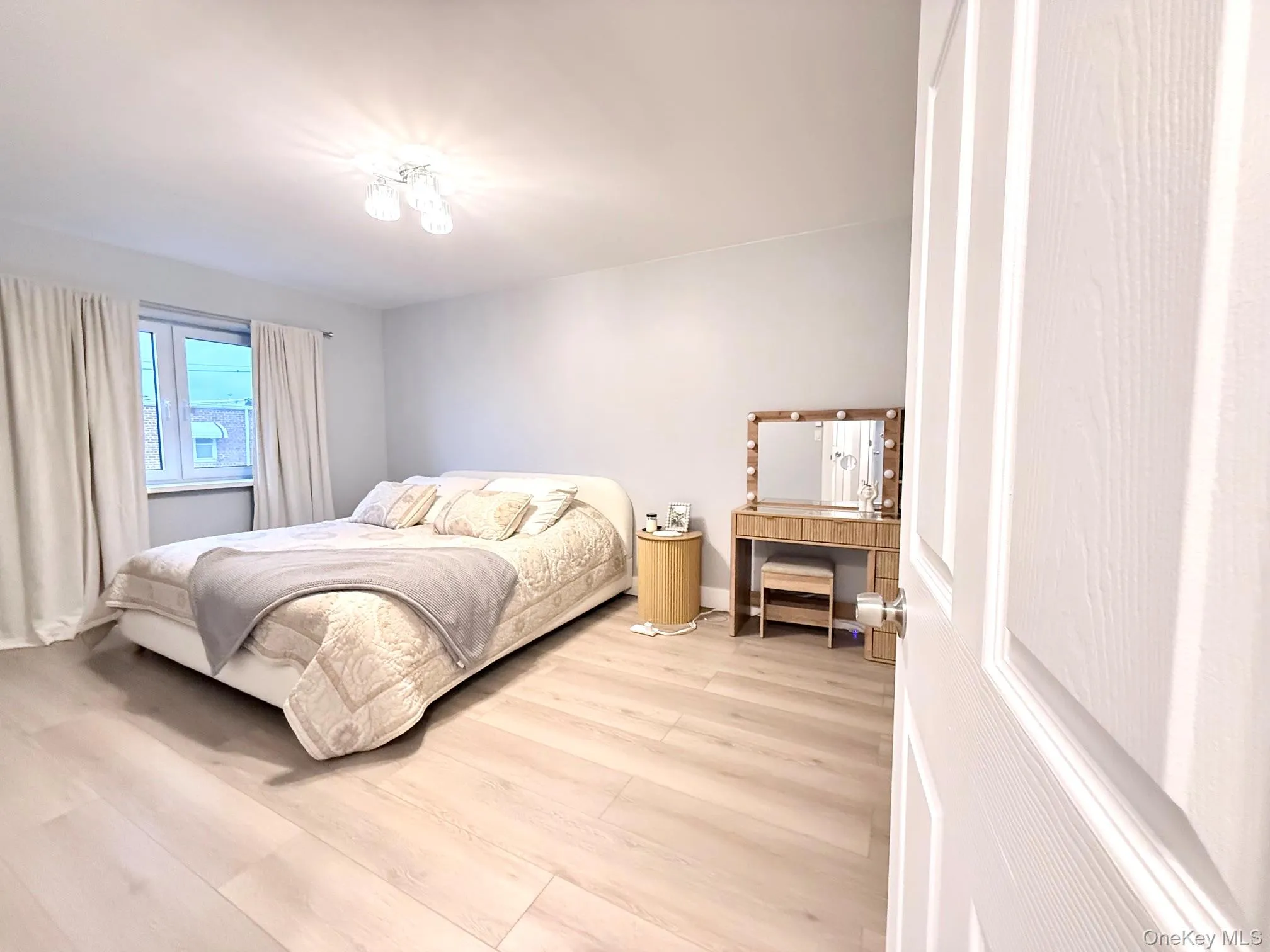Light wood-finish flooring, a contemporary ceiling light fixture, and a window with neutral drapes Light wood-finish flooring, a contemporary ceiling light fixture, and a window with neutral drapes