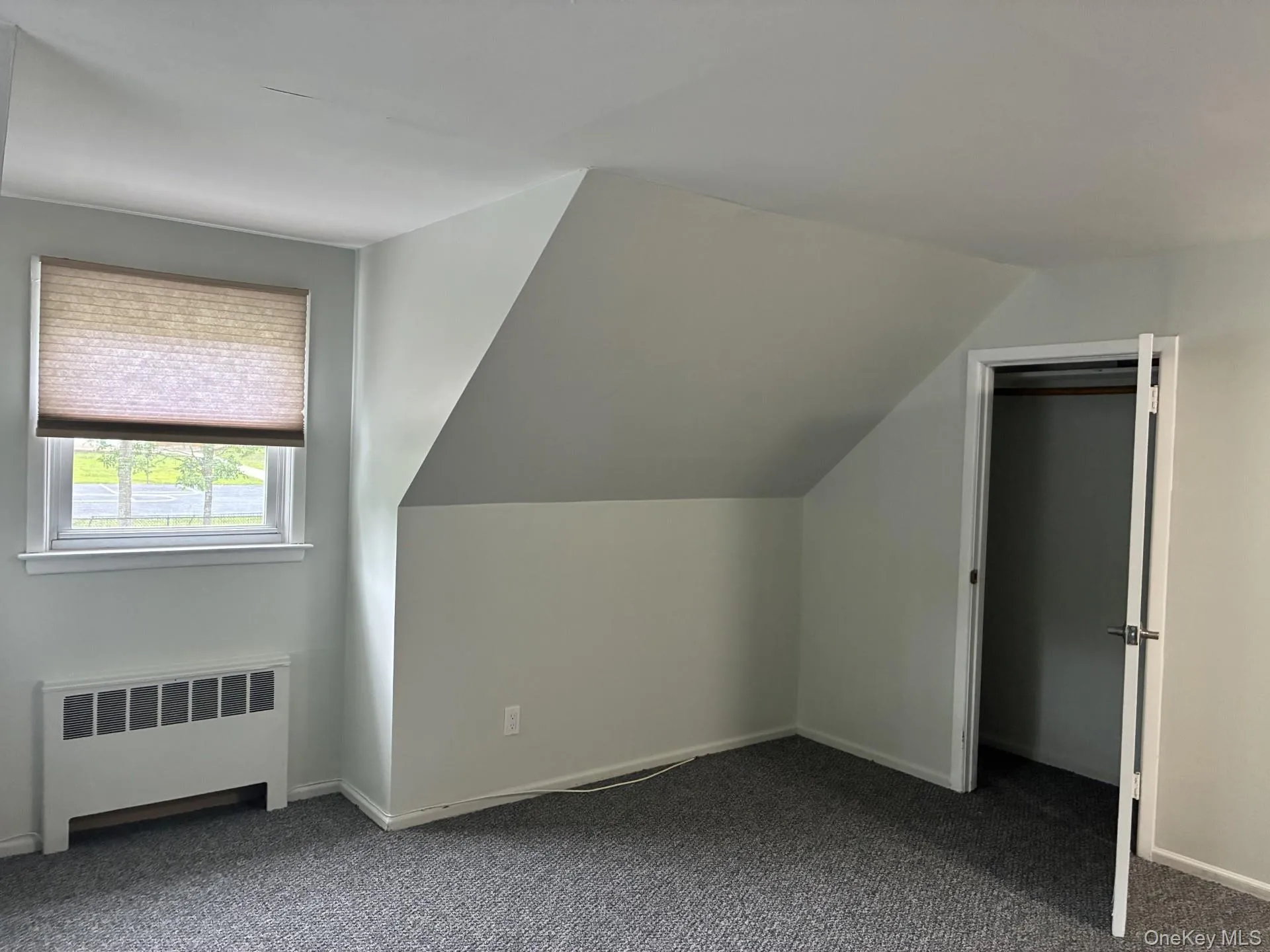 Window with cellular shade, heating unit, sloped ceiling, and closet with door Window with cellular shade, heating unit, sloped ceiling, and closet with door