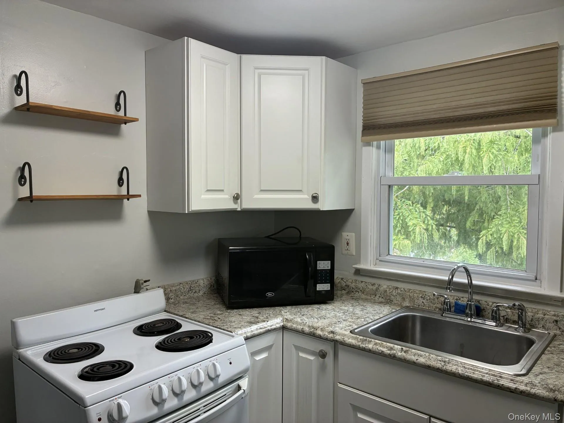 White cabinetry with brushed nickel hardware, speckled countertops, stainless steel sink with chrome faucet, and wood-finish open shelving White cabinetry with brushed nickel hardware, speckled countertops, stainless steel sink with chrome faucet, and wood-finish open shelving