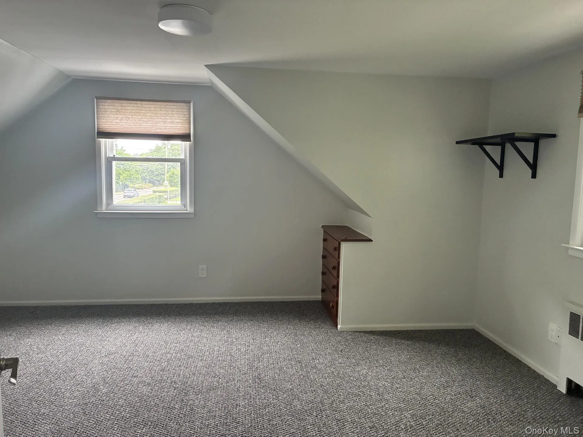 Sloped ceiling room featuring a window with cellular shades, a flush mount ceiling light, and wall-to-wall carpeting Sloped ceiling room featuring a window with cellular shades, a flush mount ceiling light, and wall-to-wall carpeting